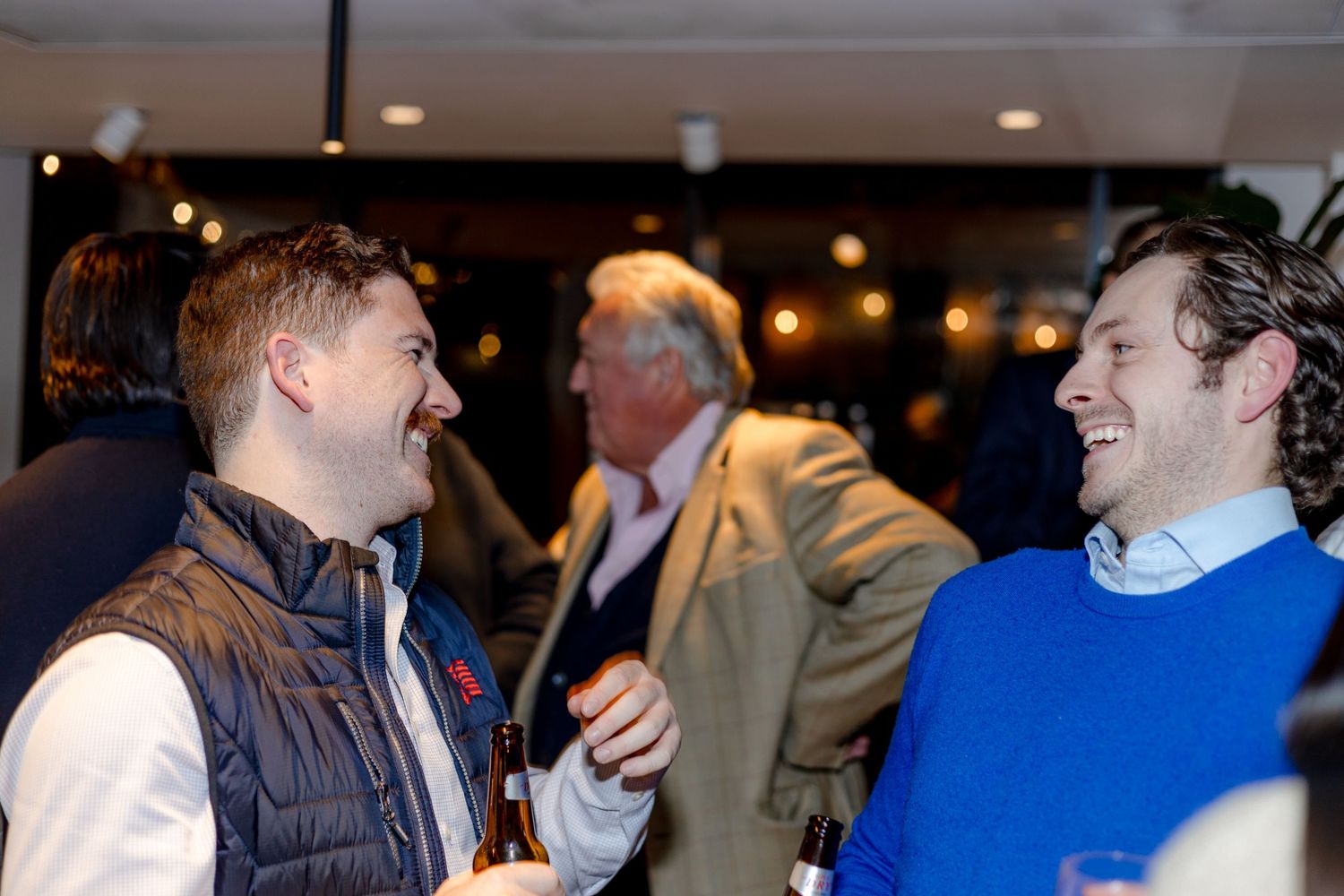 Two people sharing a laugh while conversing at an indoor social event.