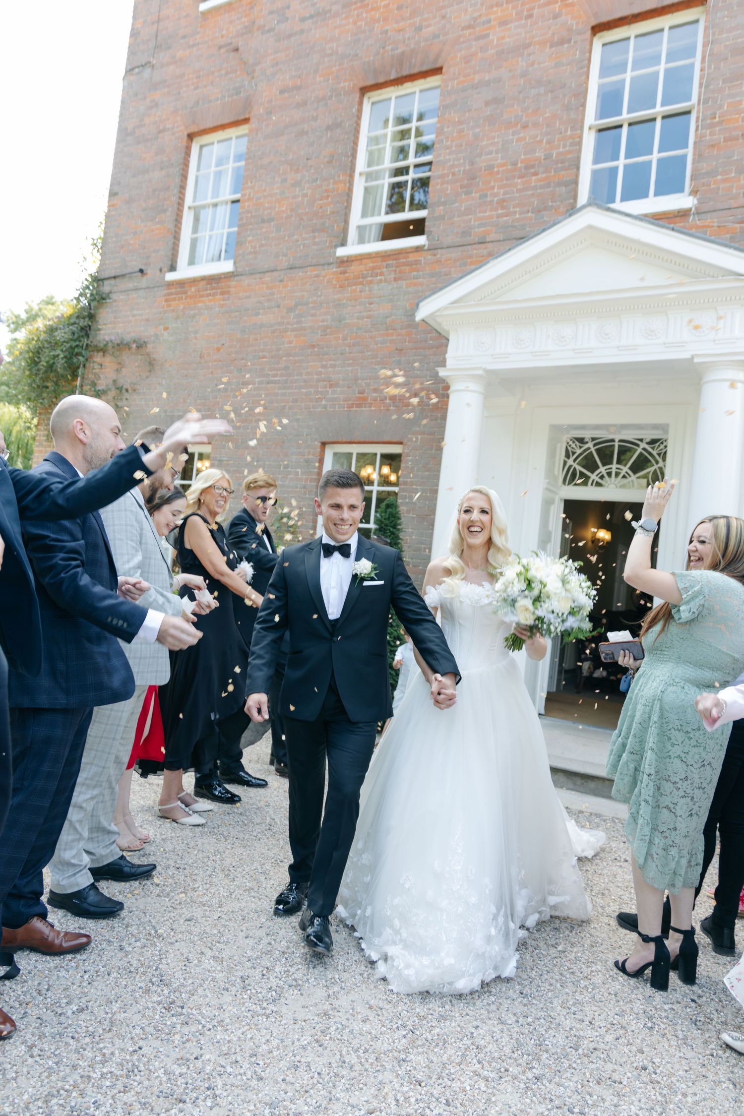 Wedding party exit celebration with guests throwing confetti outside a brick building entrance.