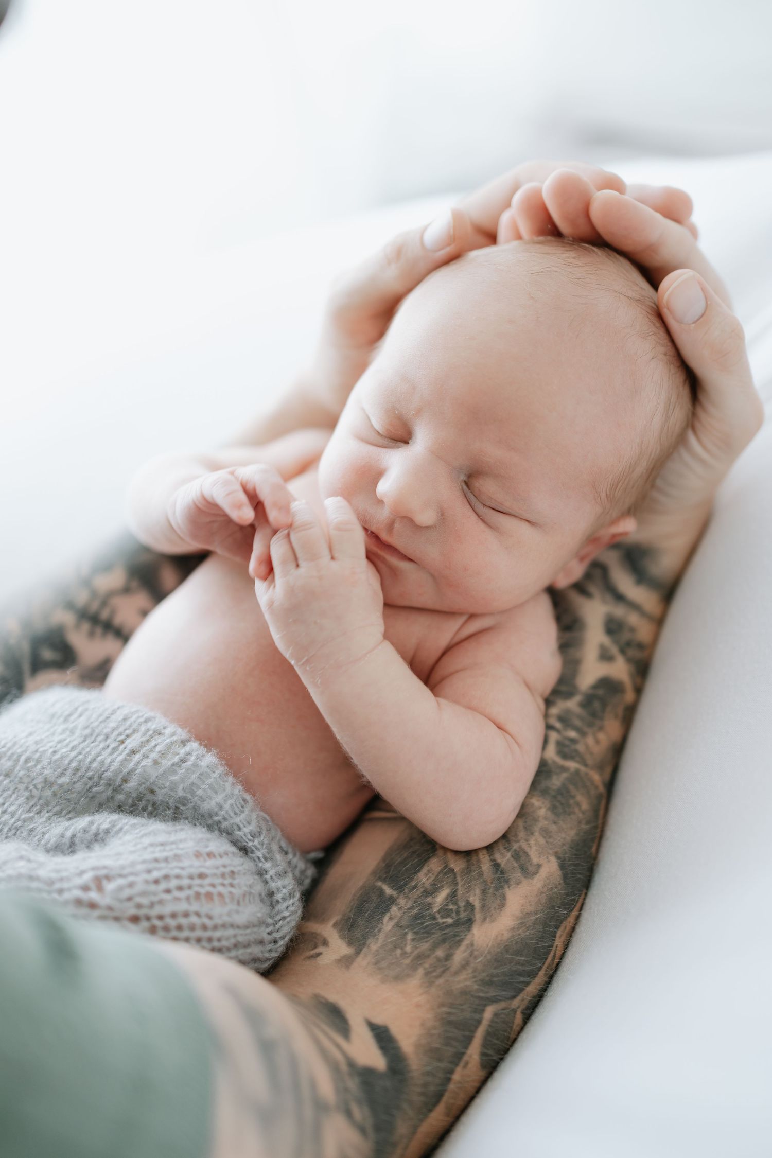 Sleeping newborn cradled on tattooed arm in intimate portrait session.