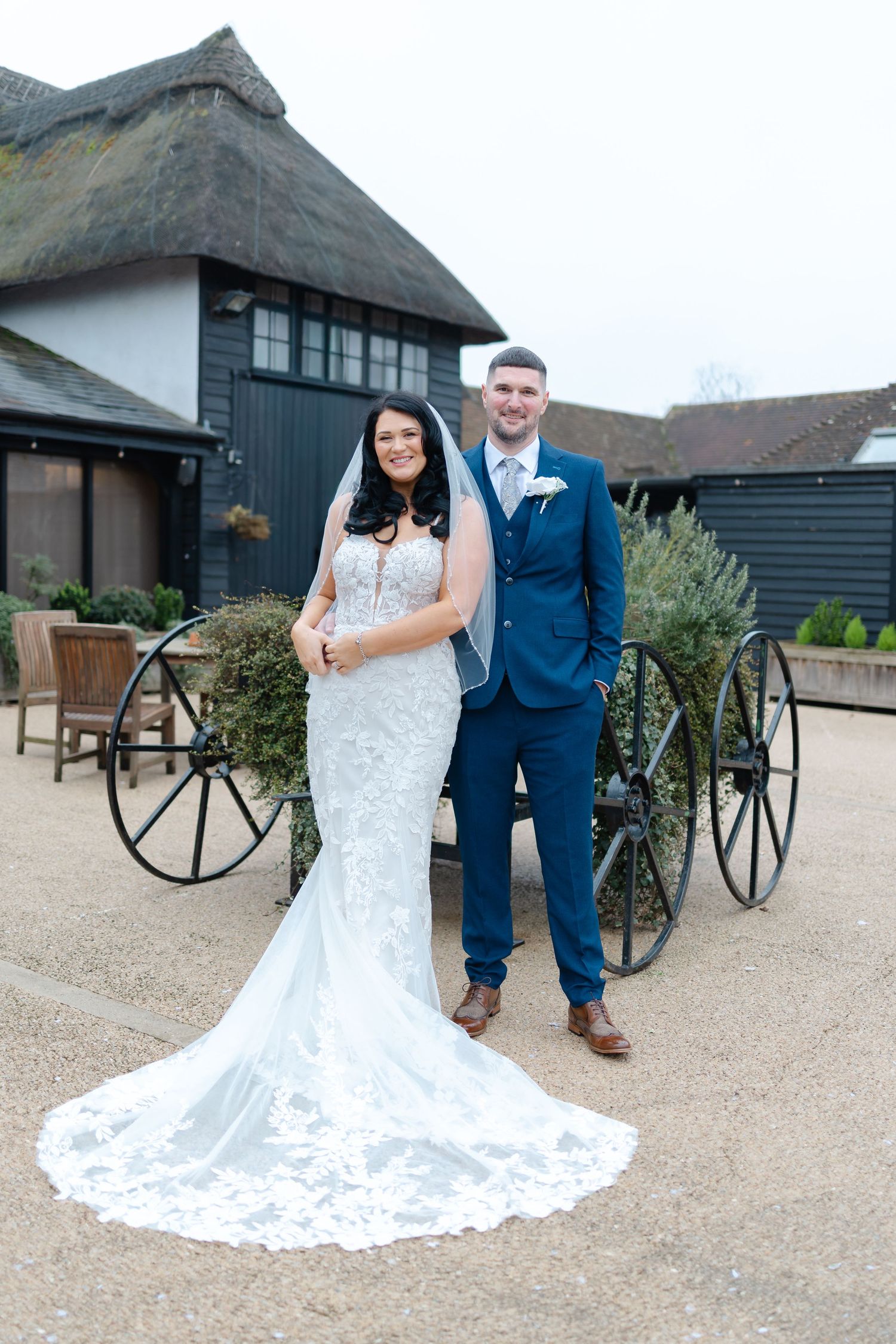 Romantic wedding portraits at a rustic venue with vintage wagon wheels in the background.