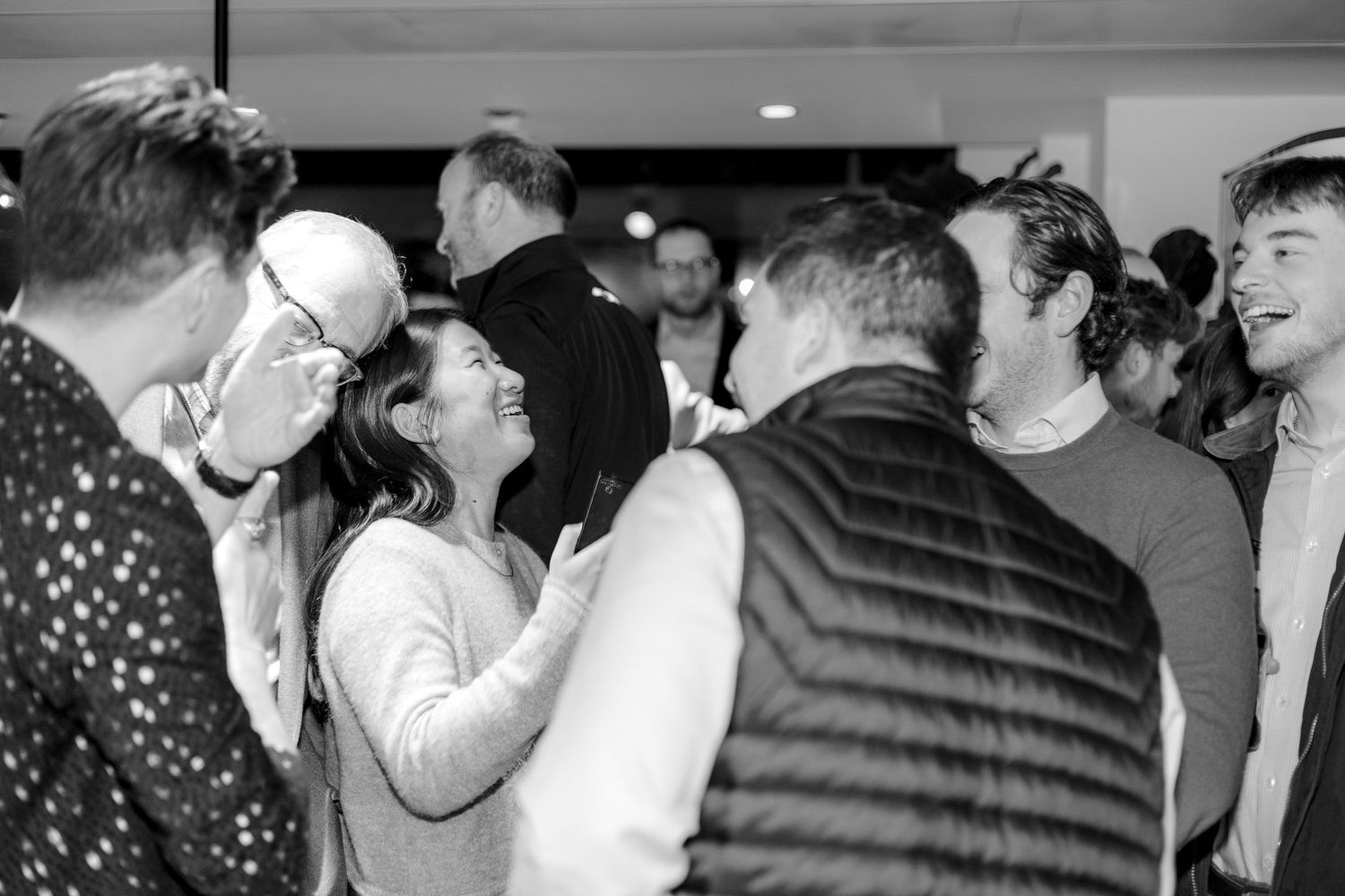 A black and white photo of people engaged in animated conversation at a social event.