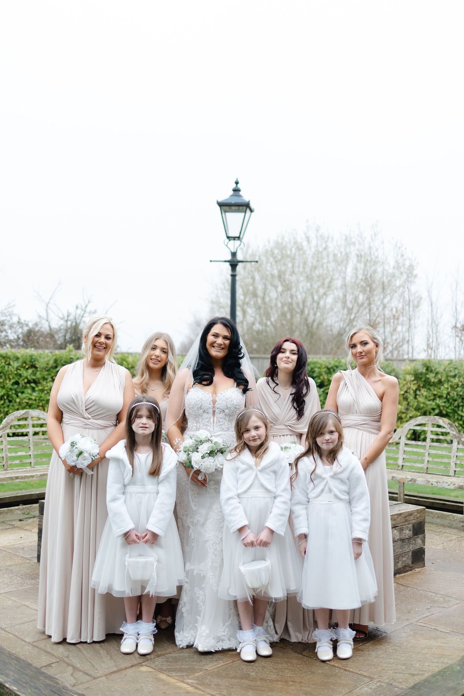 Bridal party in white and cream dresses pose together on outdoor patio.