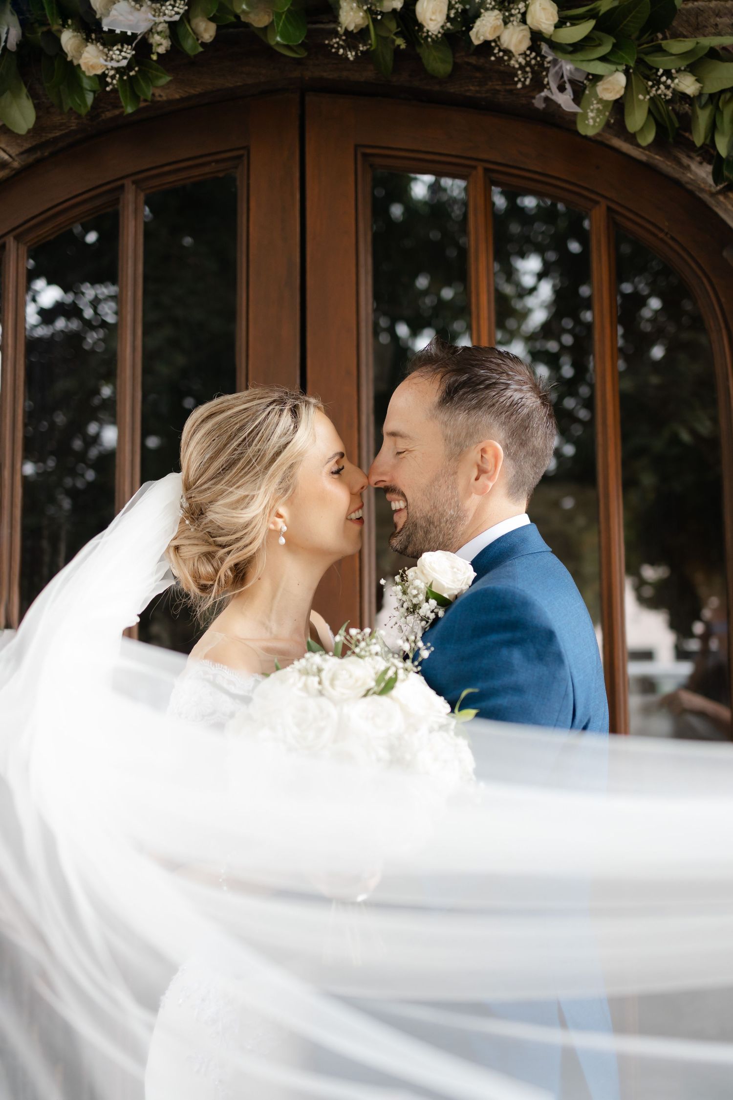 Romantic wedding portrait with flowing veil and white floral arch decorations.