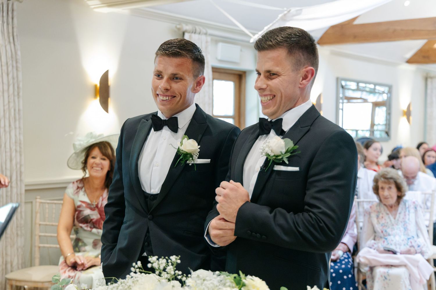 Wedding celebration scene with guests and wedding party in a bright indoor venue.