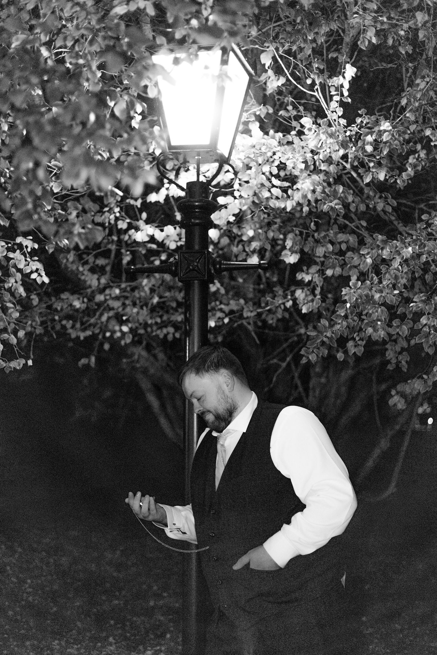 Evening wedding photography under illuminated trees and lamp post.
