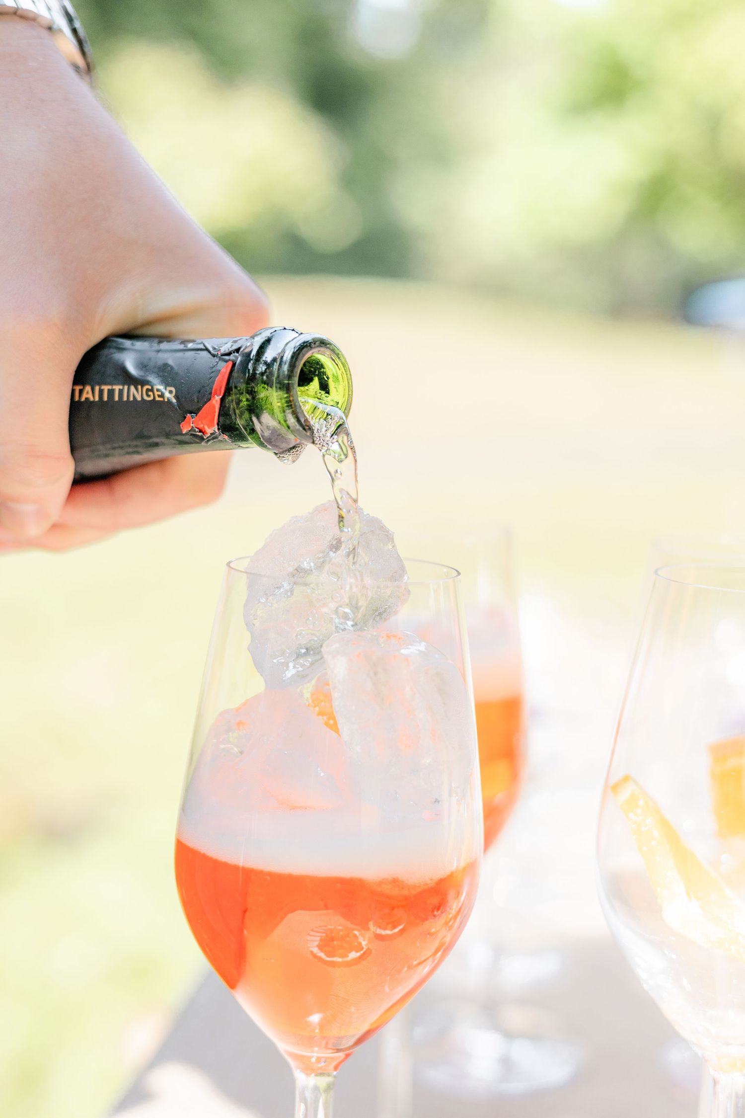 Pouring a pink sparkling beverage into an elegant wine glass outdoors.