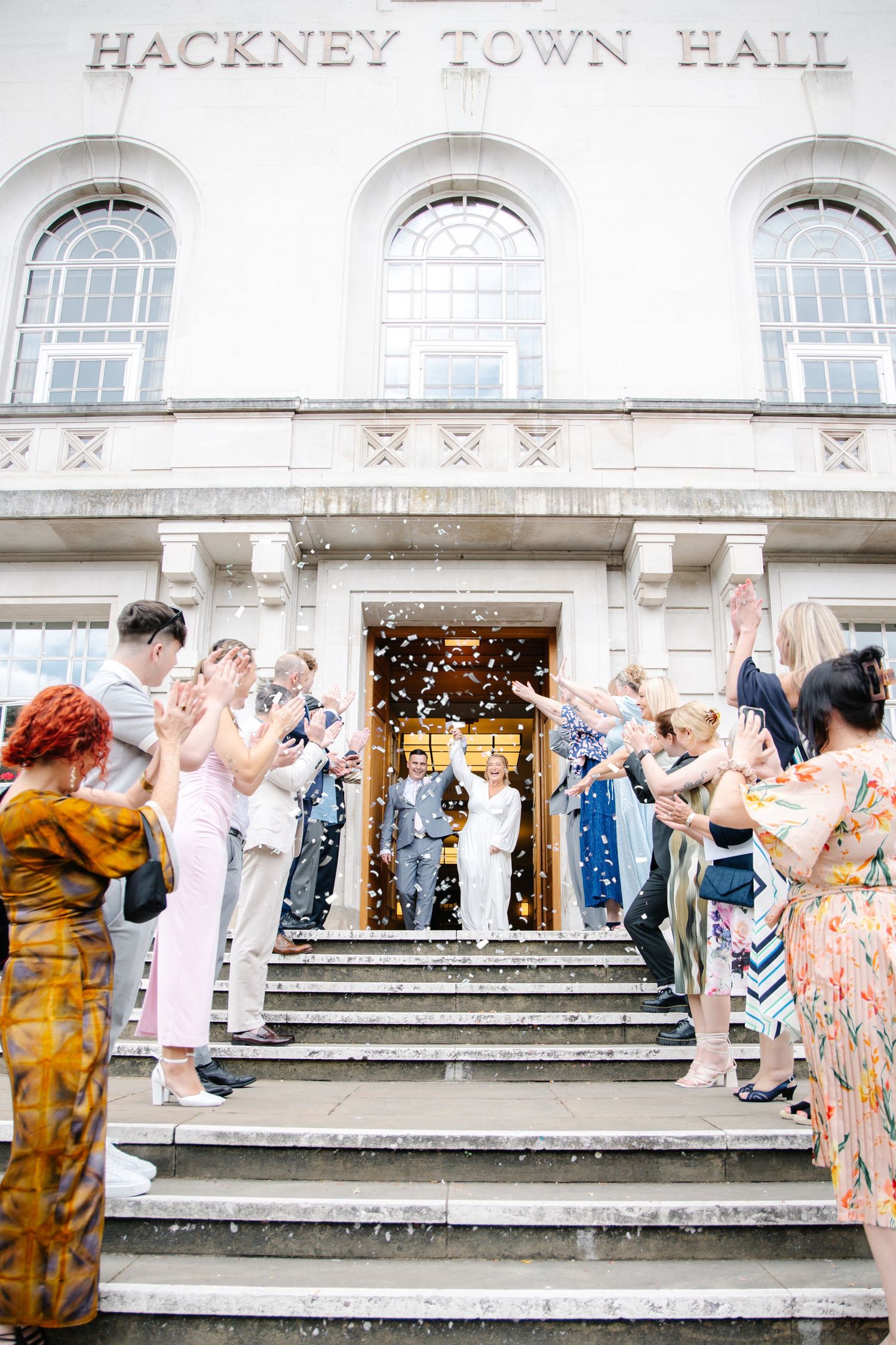 Wedding celebration on the grand steps of Hackney Town Hall with guests in colorful attire.