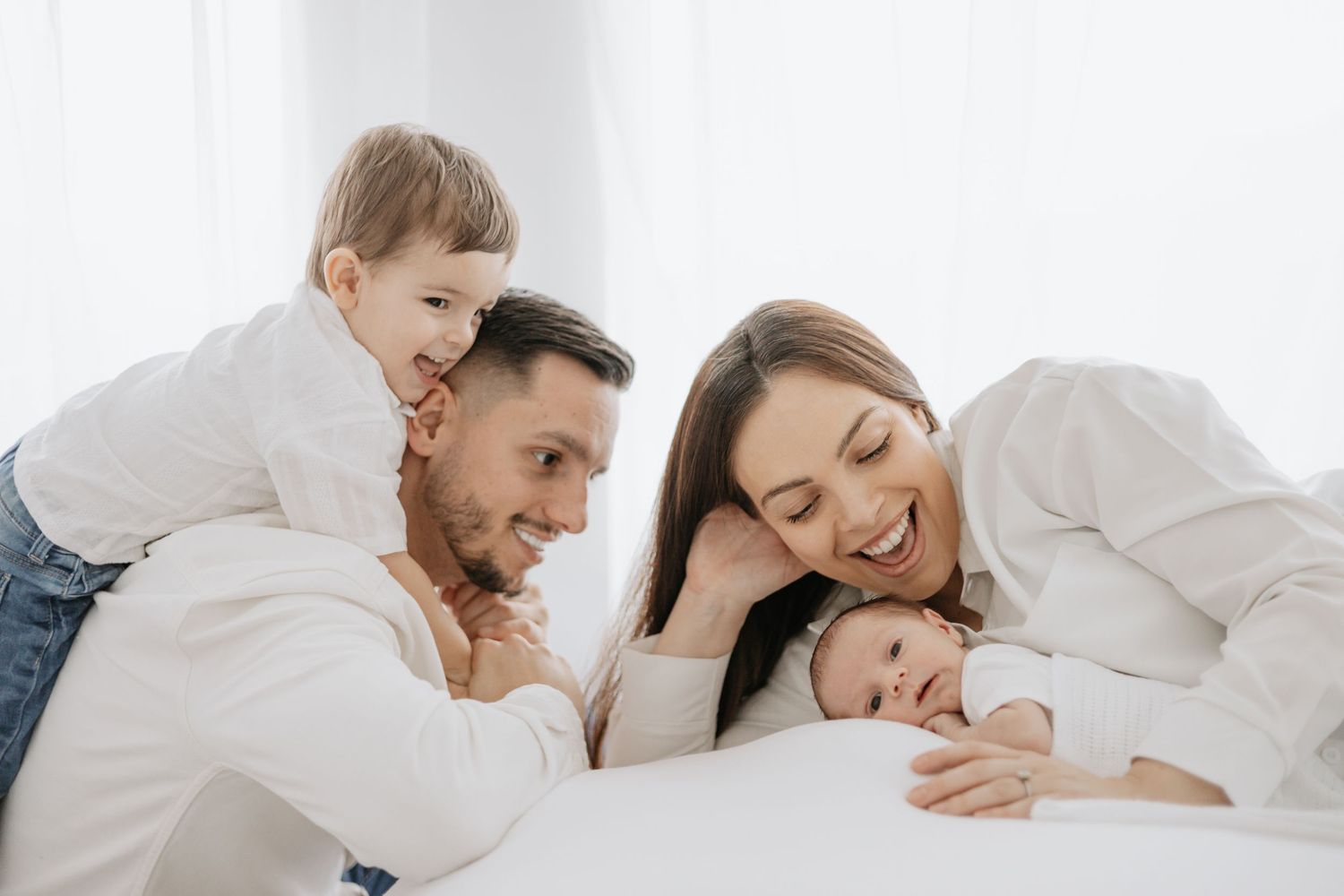Family lying together on white bedding sharing tender moments.