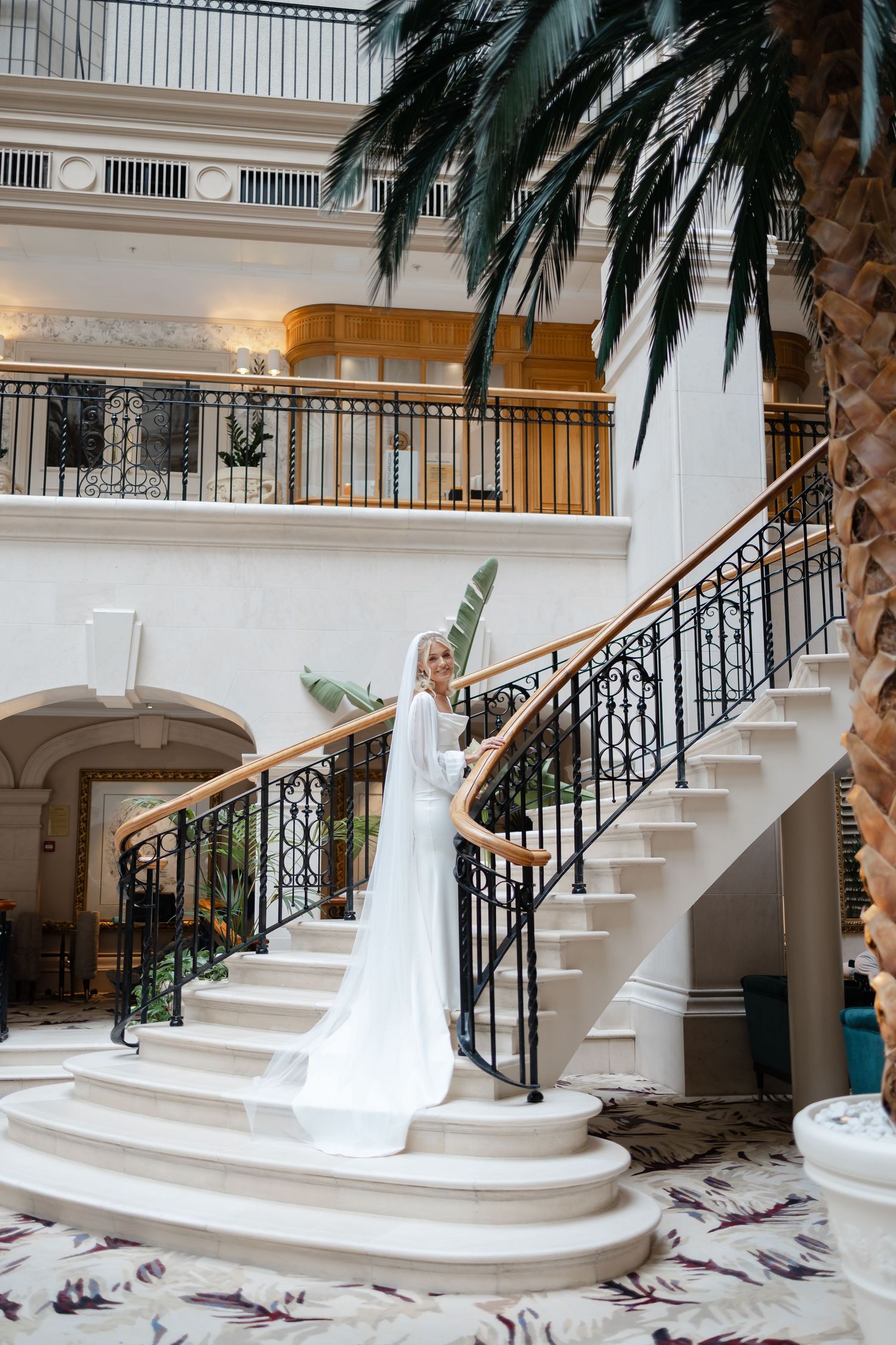 Wedding party photographed on grand white marble staircase with decorative palm trees.
