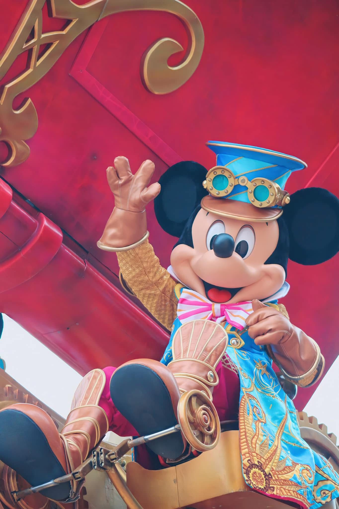 Mickey Mouse puppet performs with animated gestures against a vibrant red background at a Disney show.