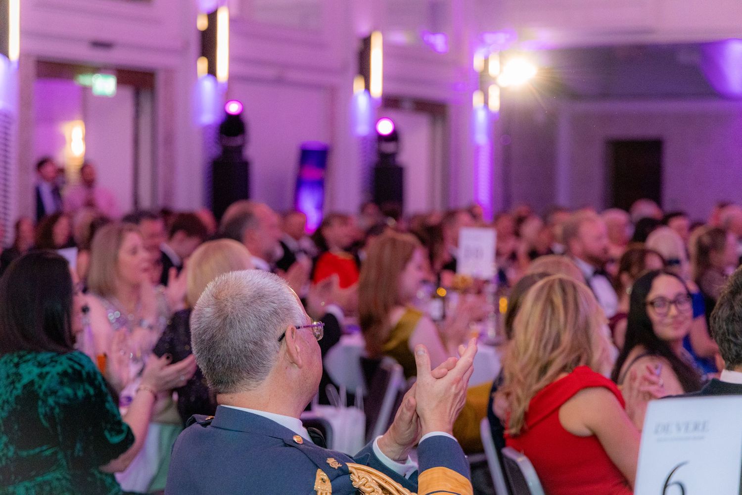 Audience members applauding during a formal event with purple ambient lighting.