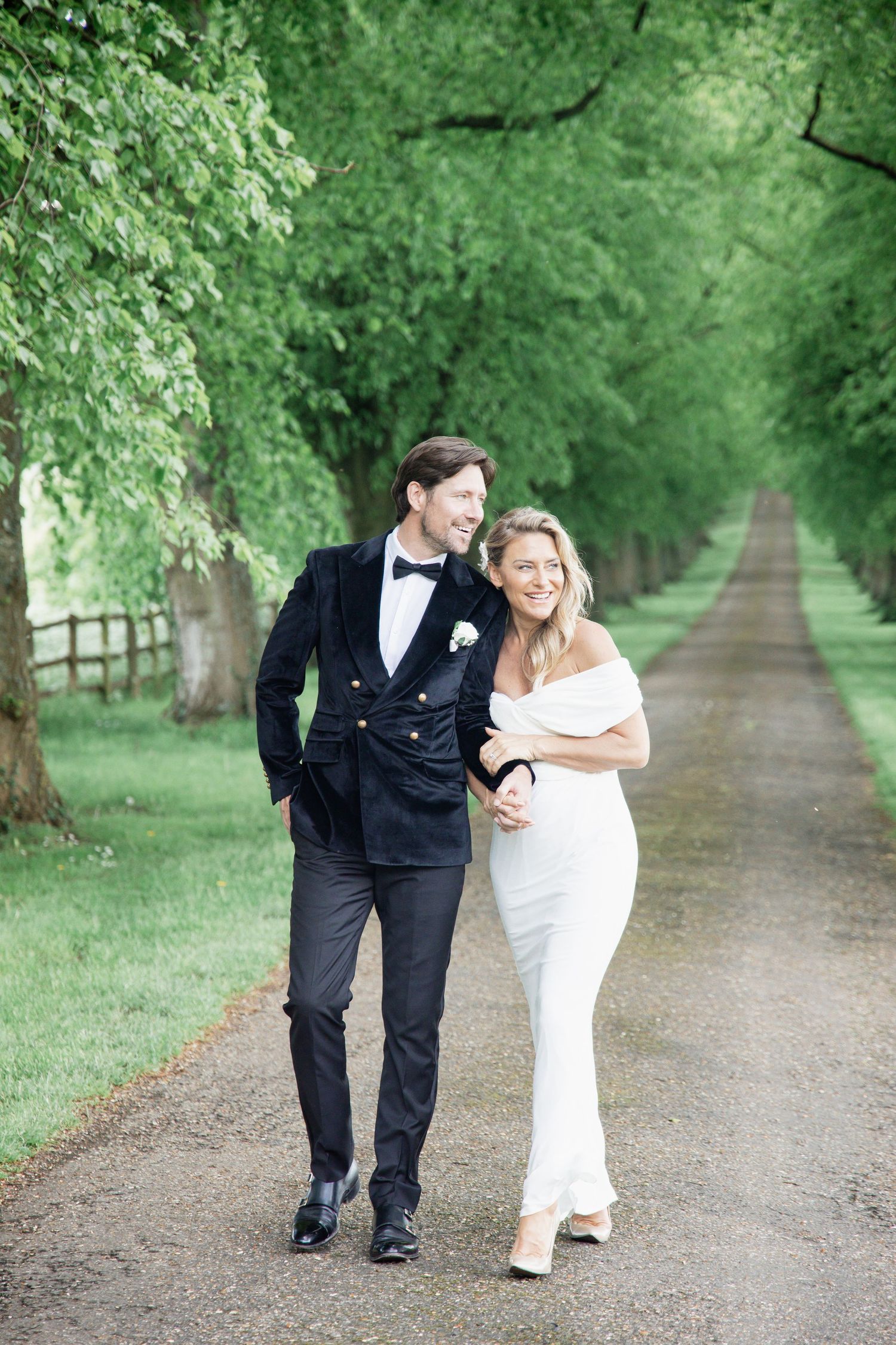A couple shares a tender moment while walking along a scenic tree-lined dirt path.