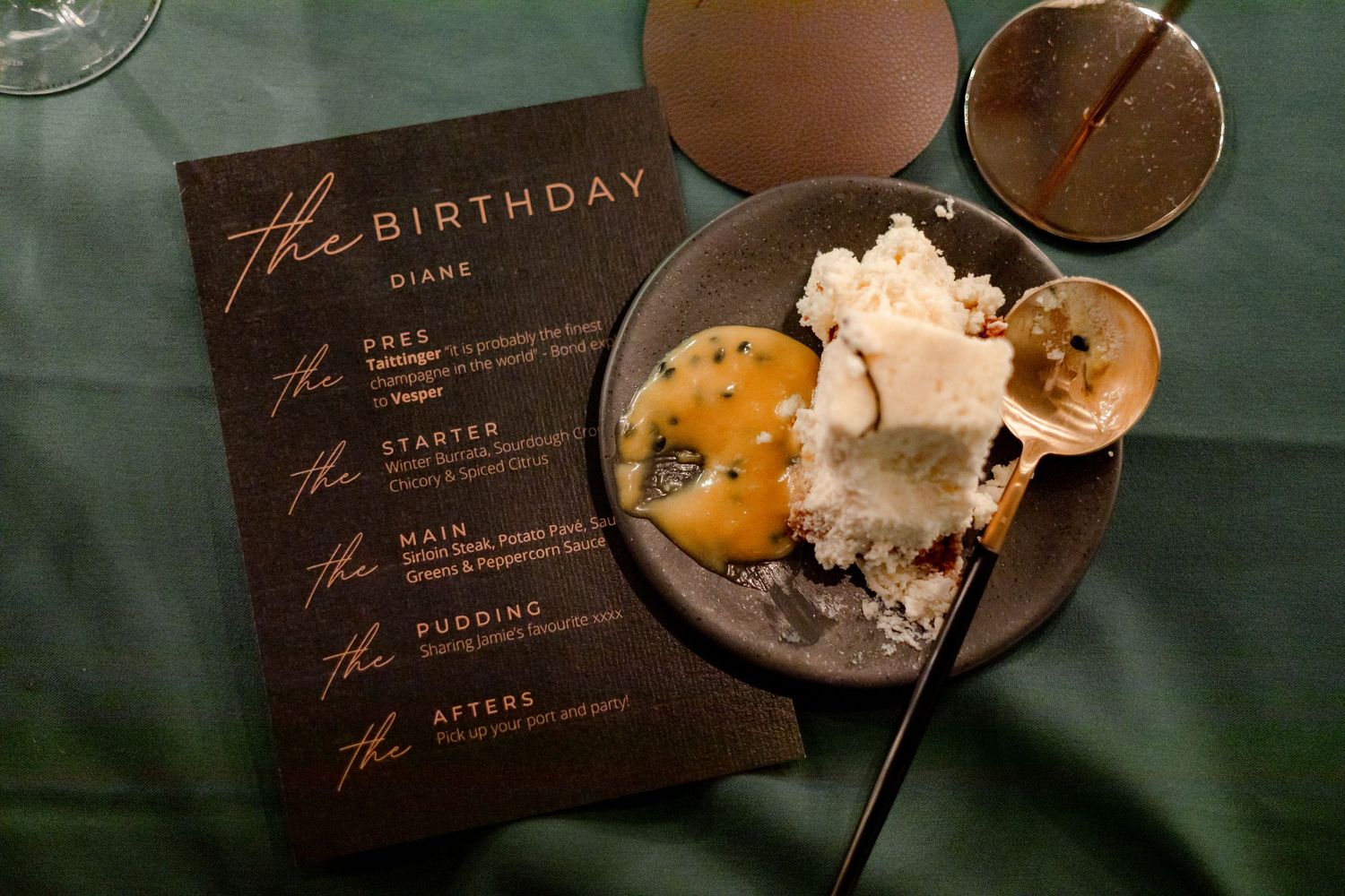 Birthday menu cards and dessert plates arranged on a dark green tablecloth.