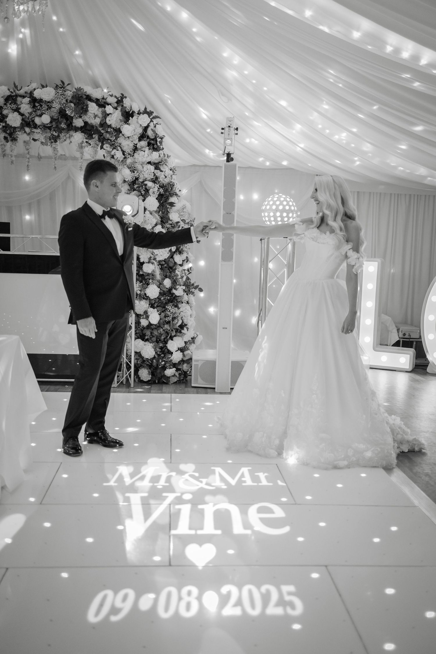Wedding reception venue with white draping, fairy lights and projected text on the dance floor.