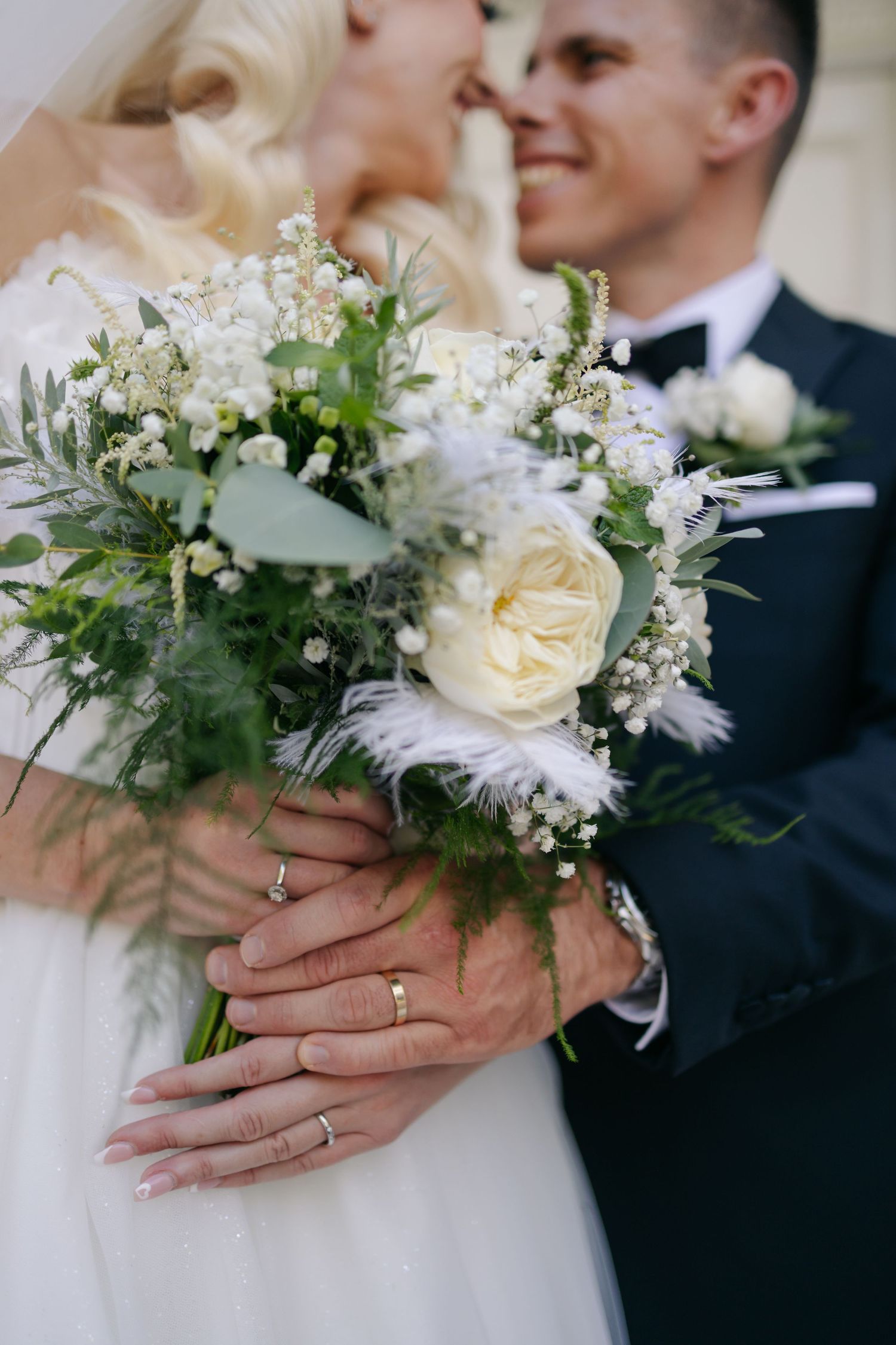Close-up of wedding bouquet with white roses and greenery held between bride and groom.