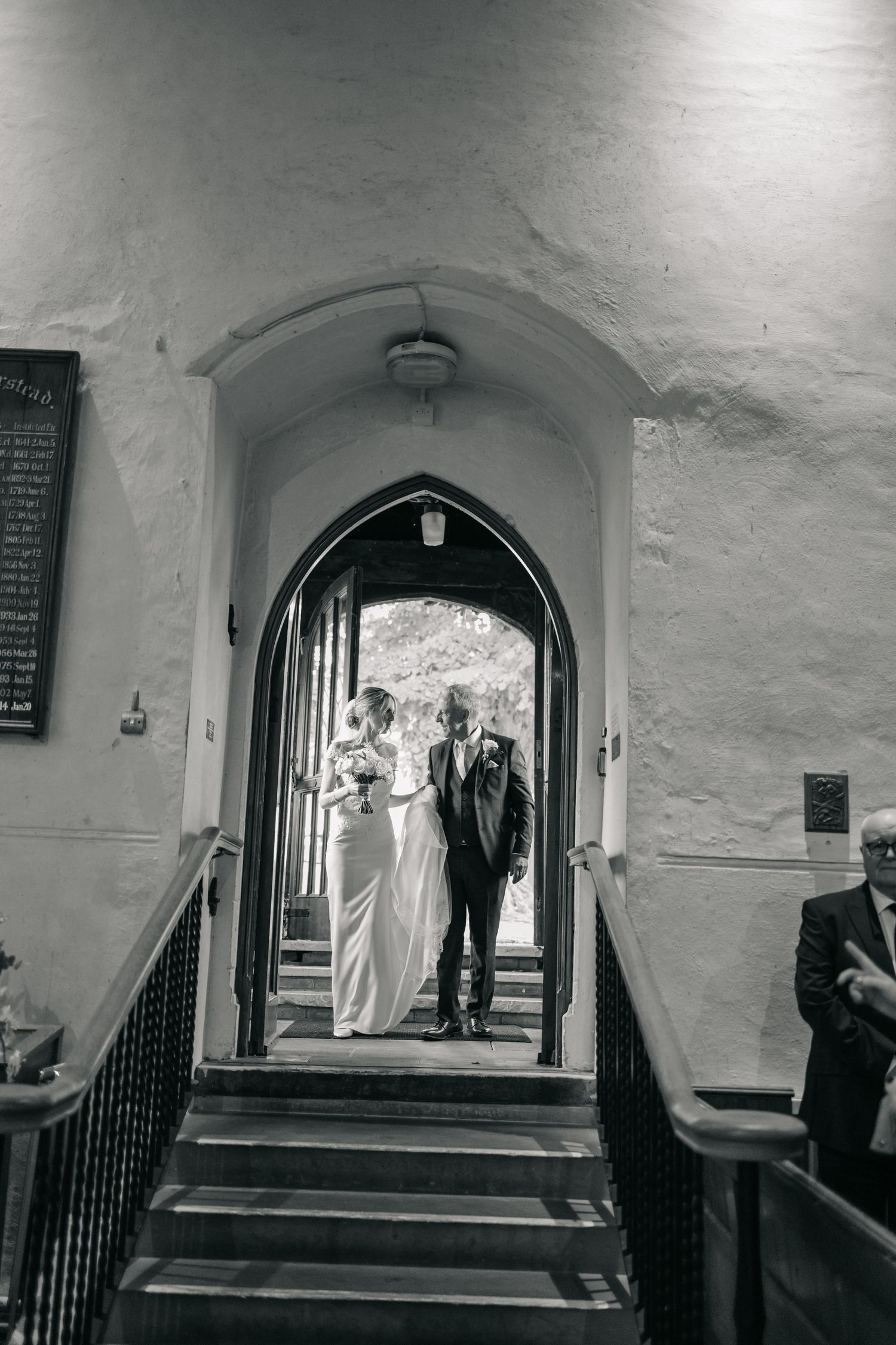 Black and white photo of couple walking through arched church hallway.