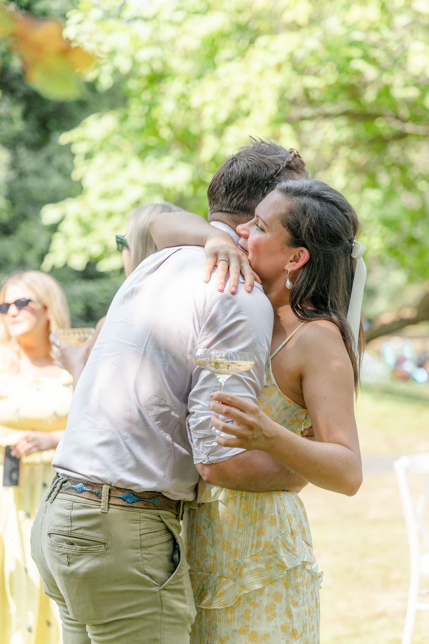 Tender embrace shared between guests during outdoor celebration with drinks.