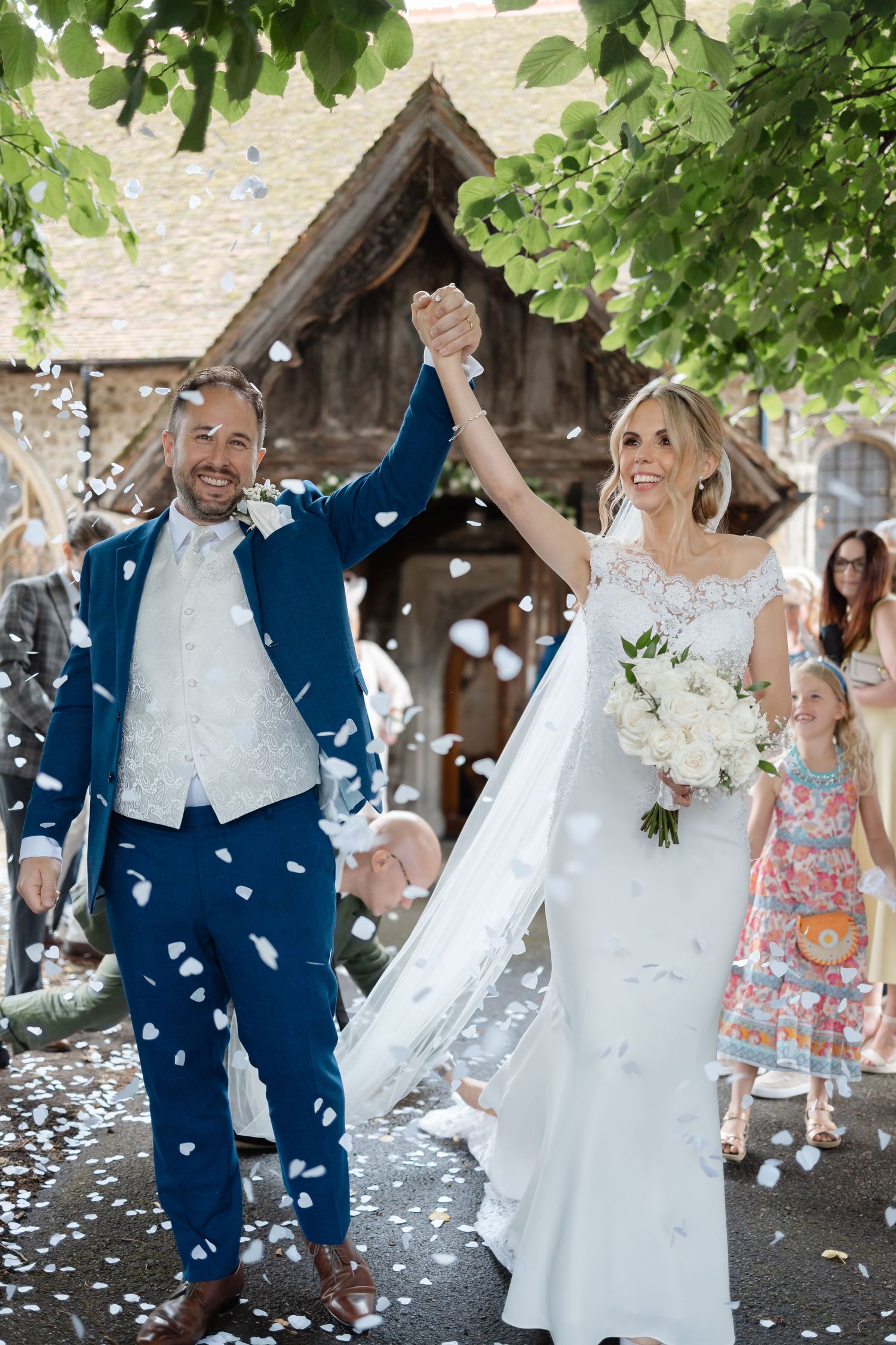 Wedding celebration with confetti shower under church entrance covered in green foliage.