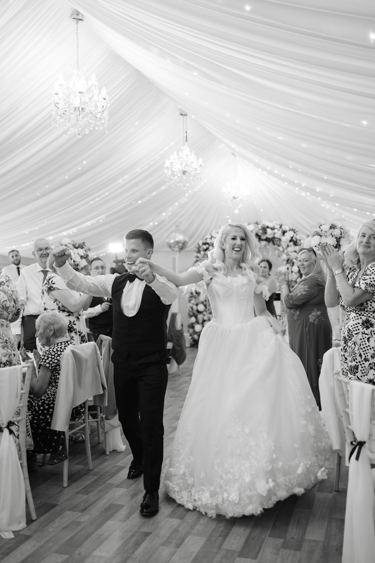 Wedding reception in elegant white draped tent with chandelier and dancing guests.