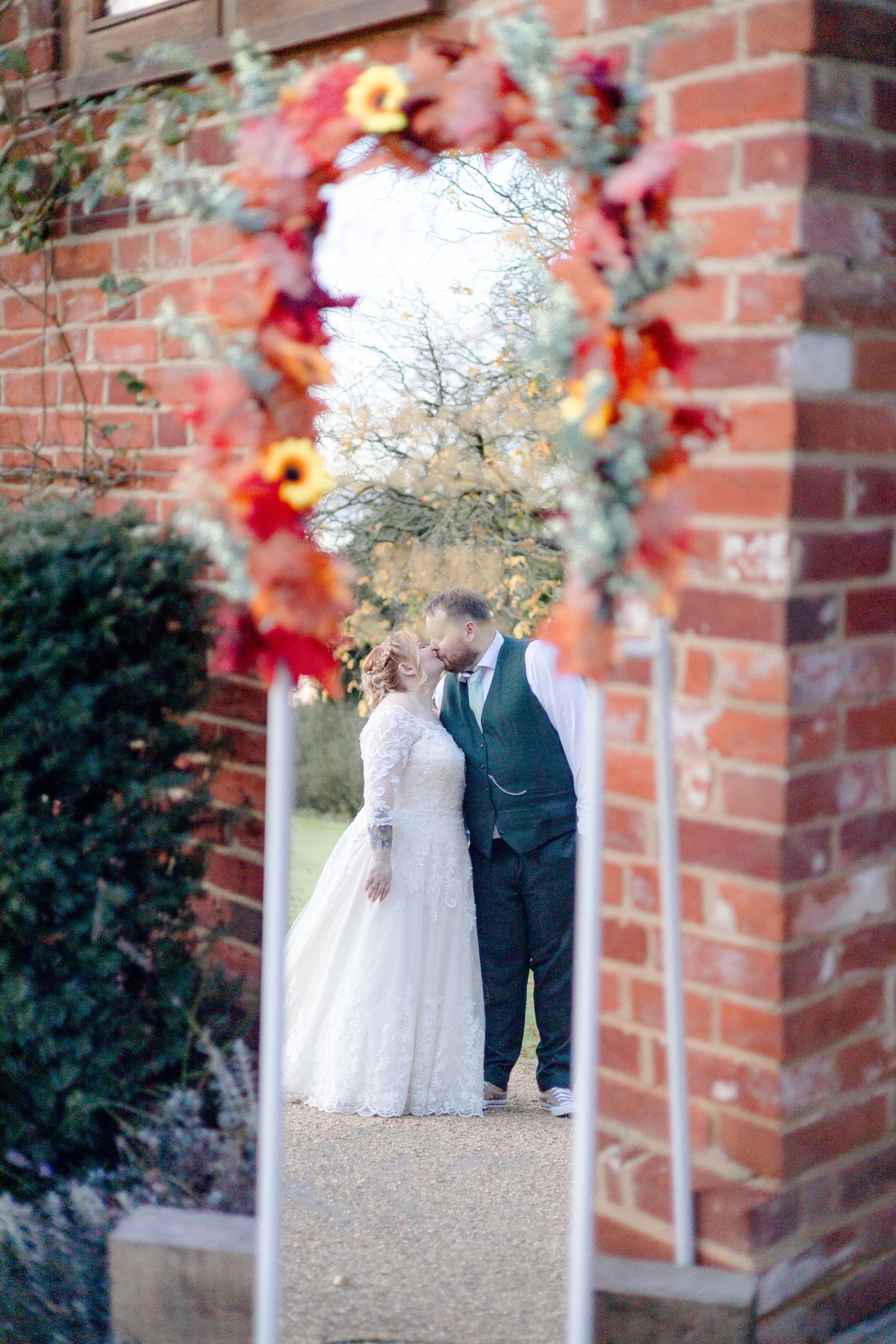 Wedding couple photographed through brick archway with autumn foliage.