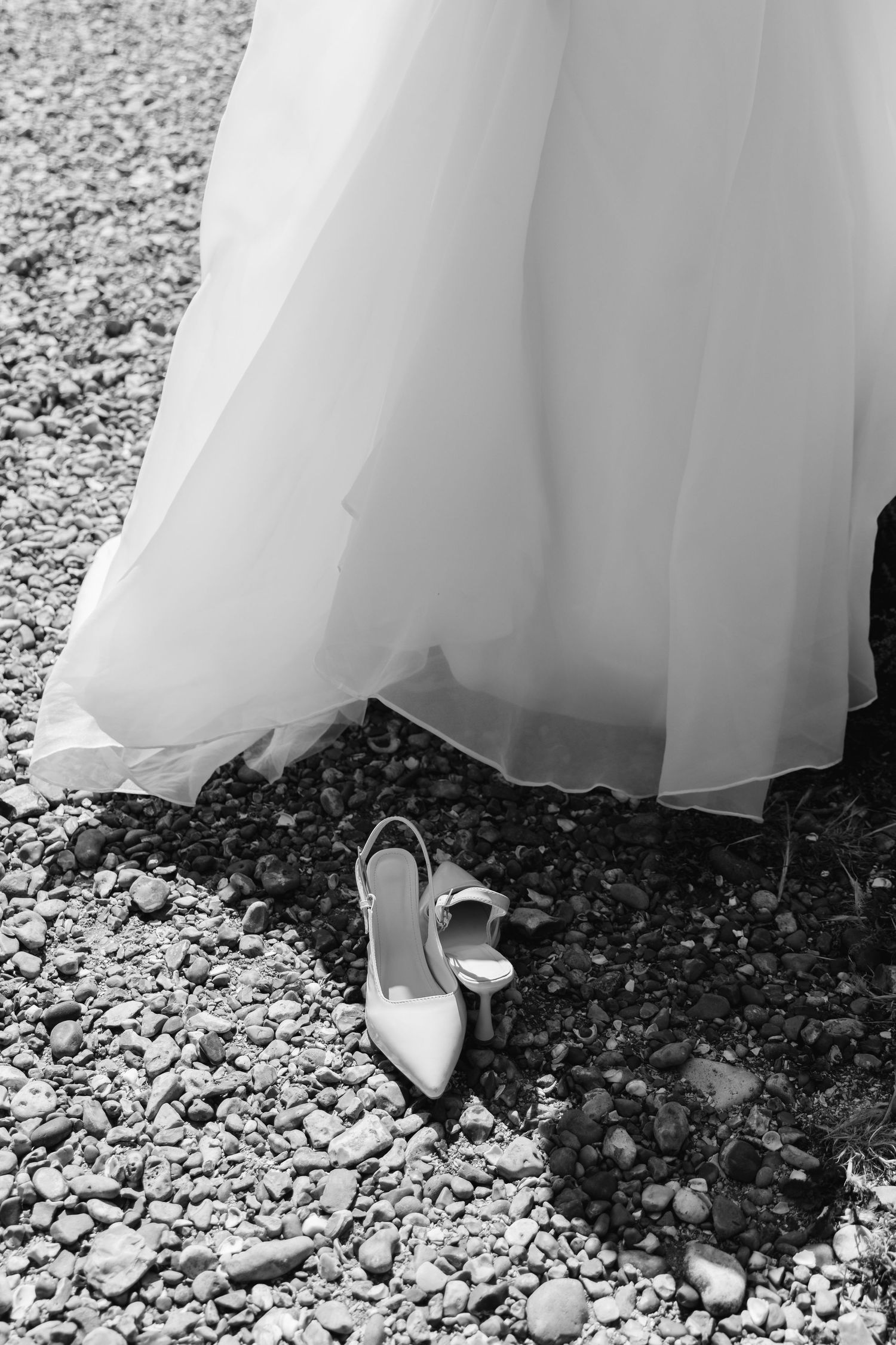 White wedding dress and silver heels on a pebbled beach.