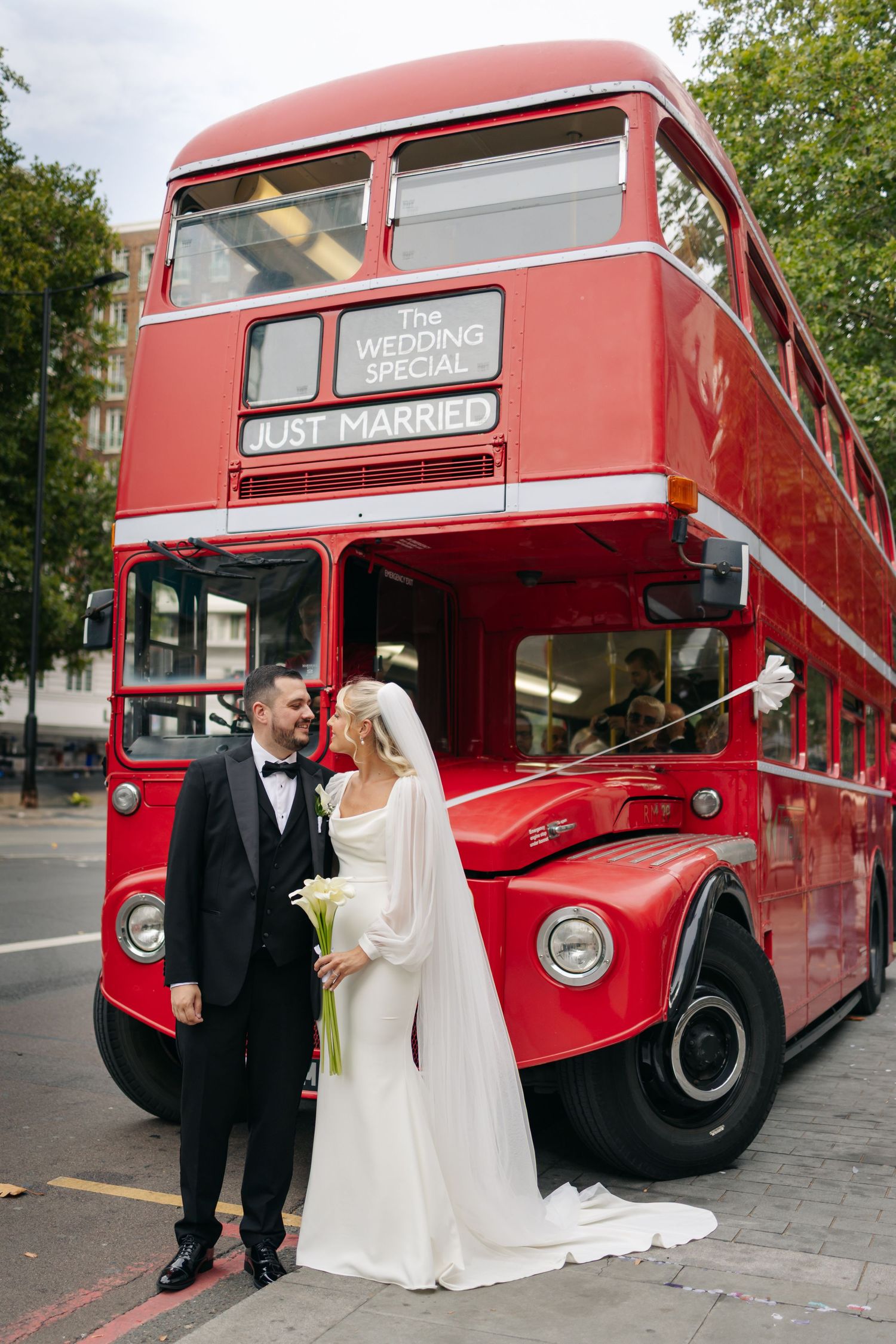 Wedding couple poses for photos with a classic red London double-decker bus.