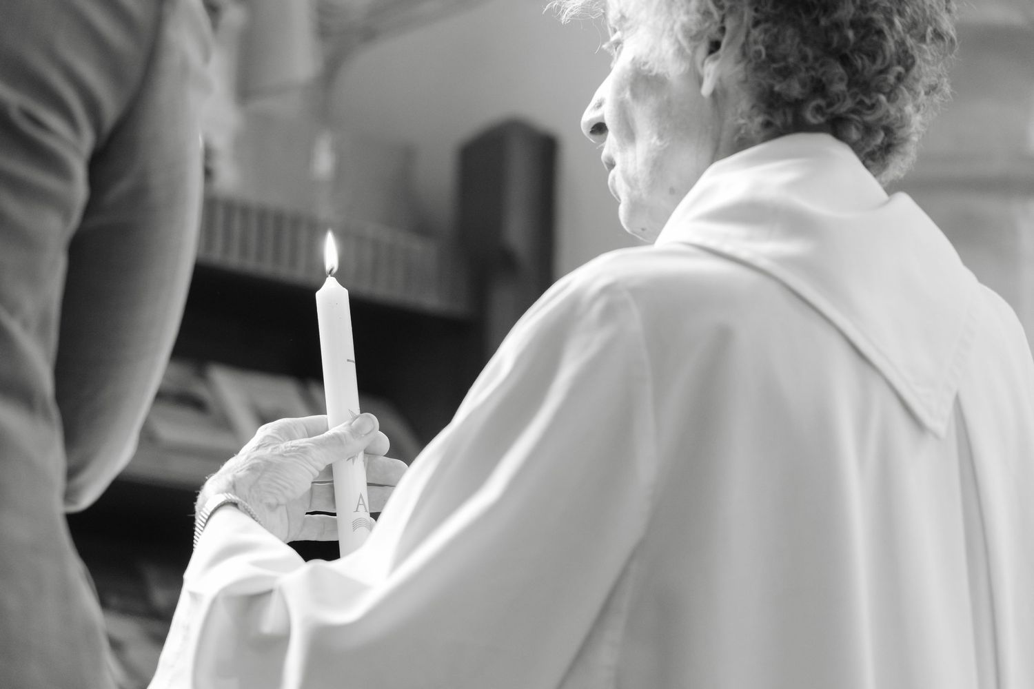 A person in white robes holds a lit candle during a religious ceremony.