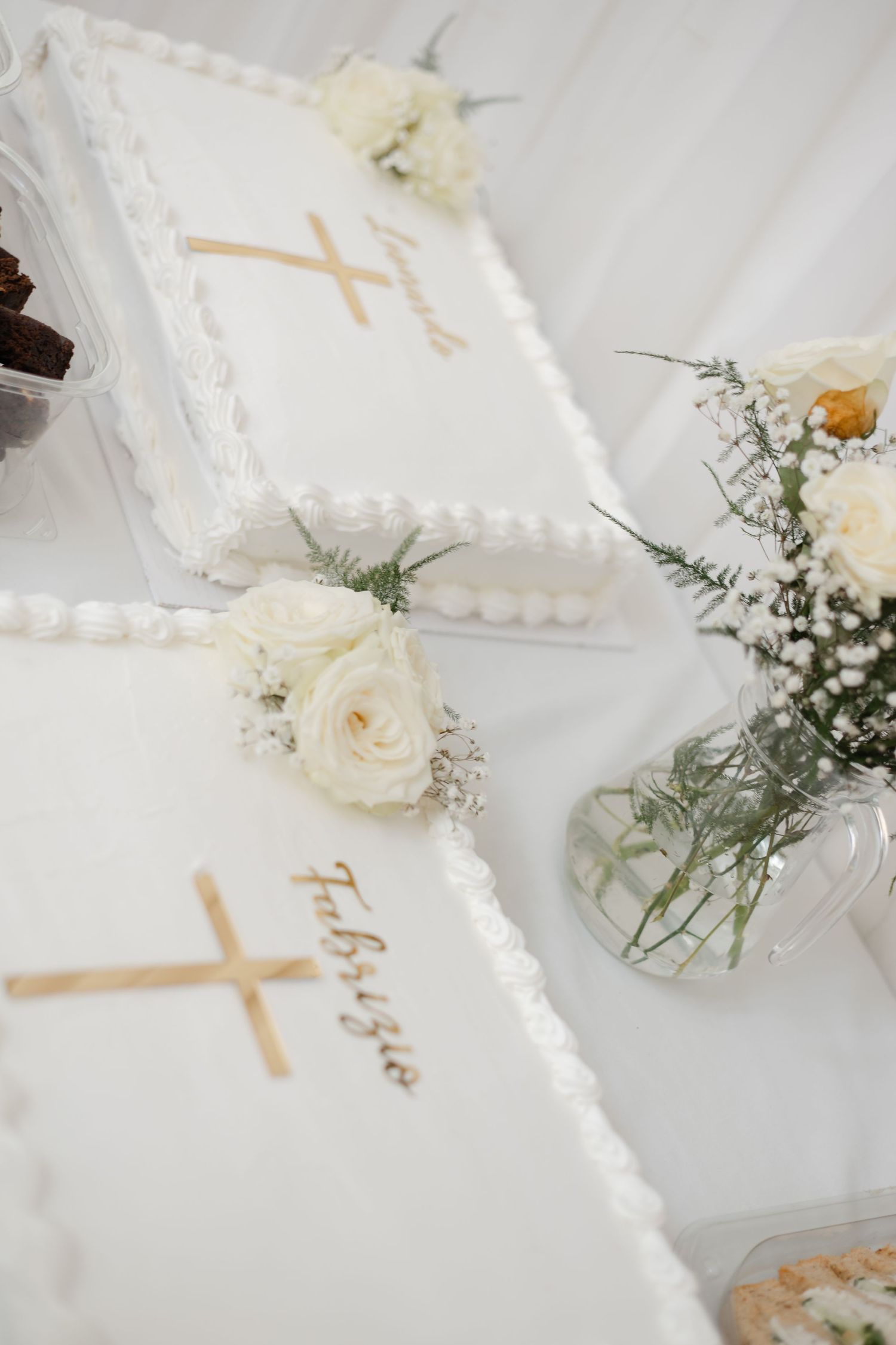 White baptism cake decorated with crosses and roses on white tablecloth.