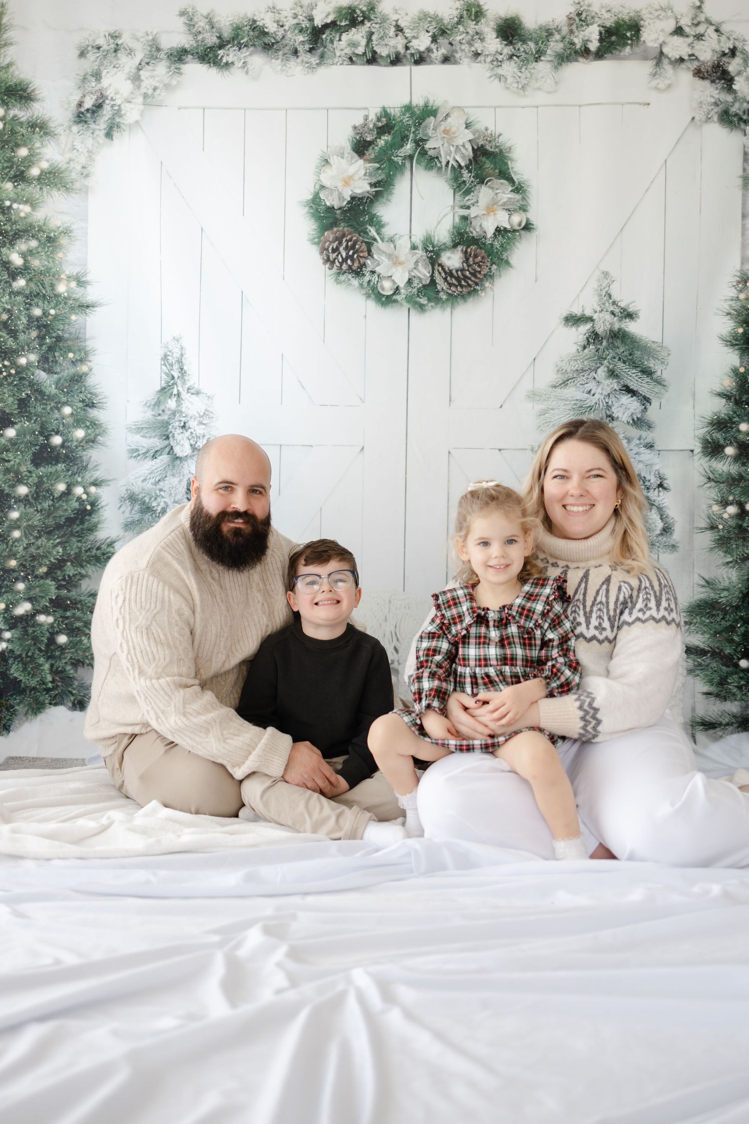 Winter holiday photo setup with white backdrop, Christmas wreath and snowy trees.