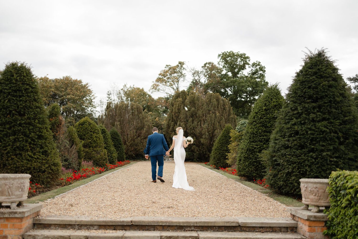 Newlyweds walking along a gravel path surrounded by evergreen trees.