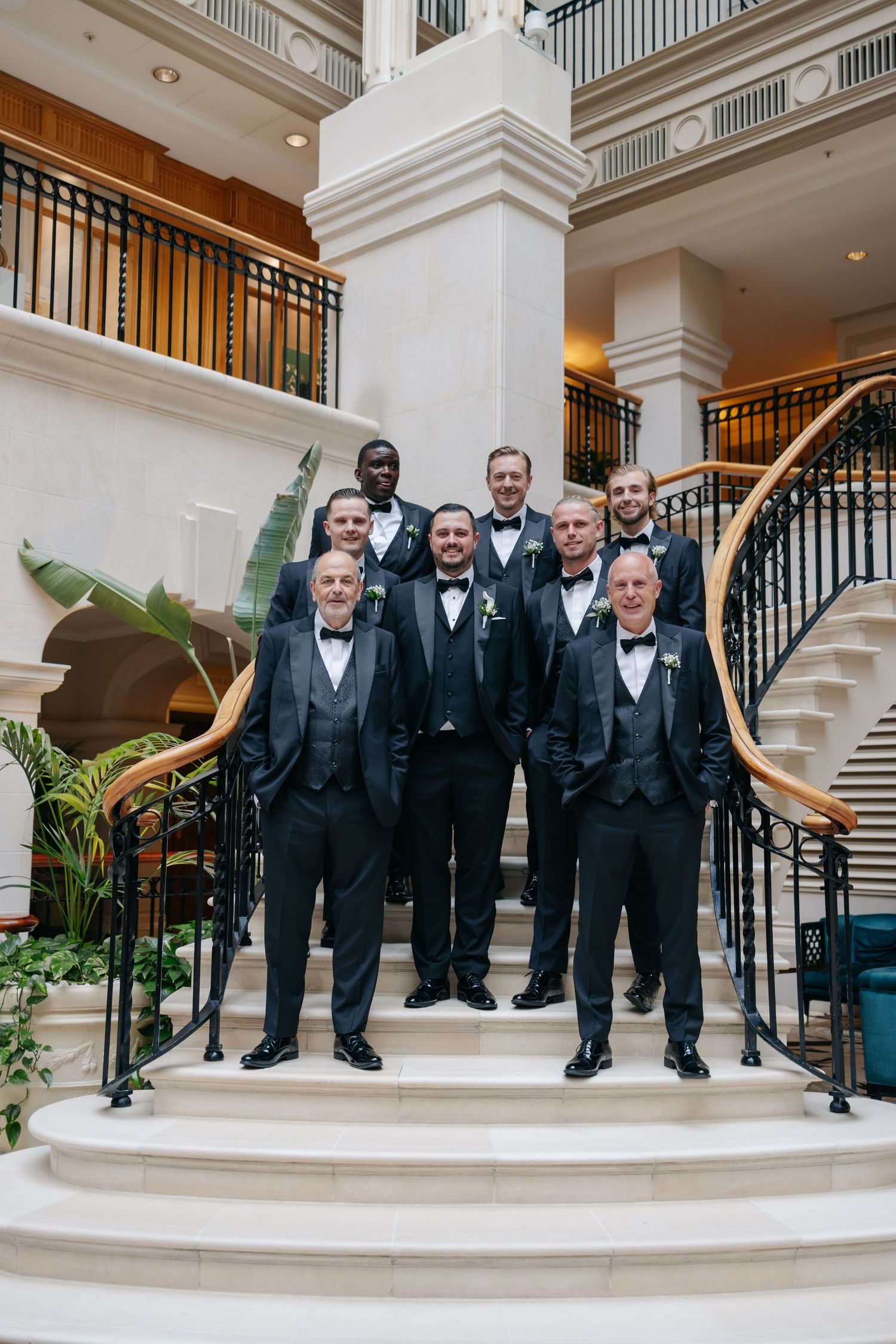 Groomsmen in matching tuxedos posing on elegant marble staircase.