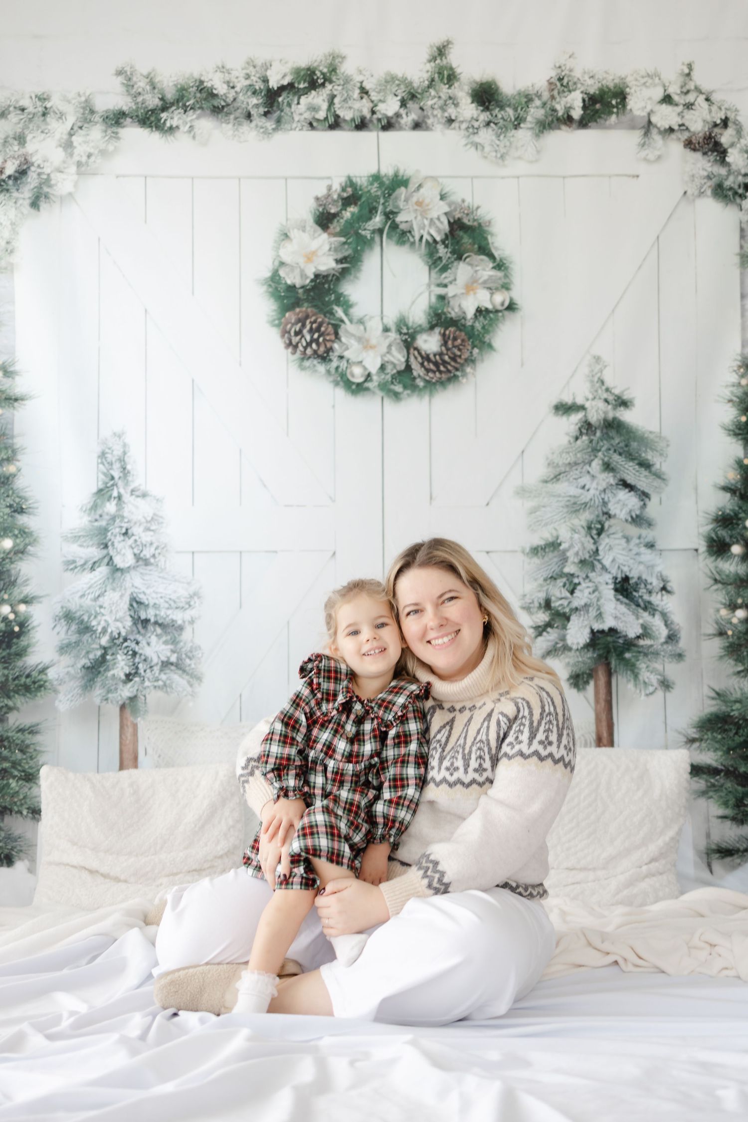 Holiday portrait with winter themed backdrop featuring wreath and snow-covered trees.
