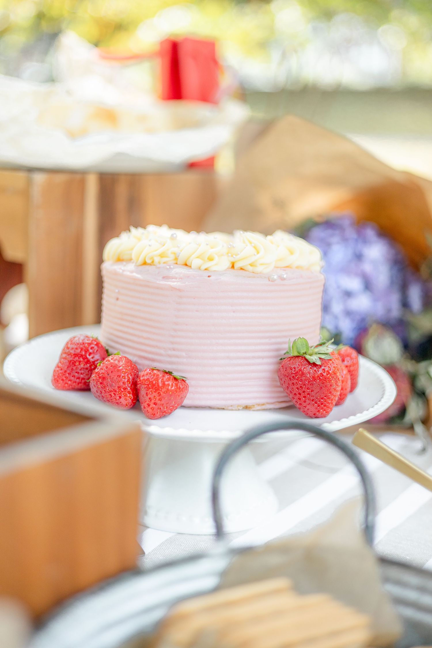 Pink frosted cake decorated with fresh strawberries and edible flowers on a white plate.