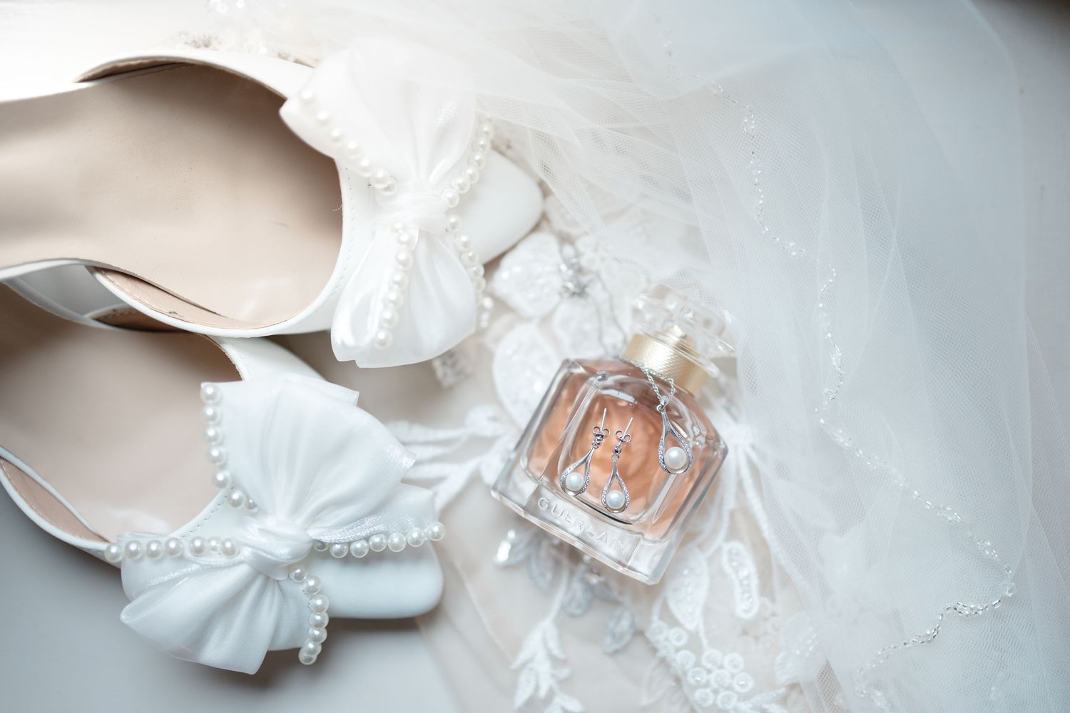 Wedding accessories including white shoes and perfume bottle arranged on light background.