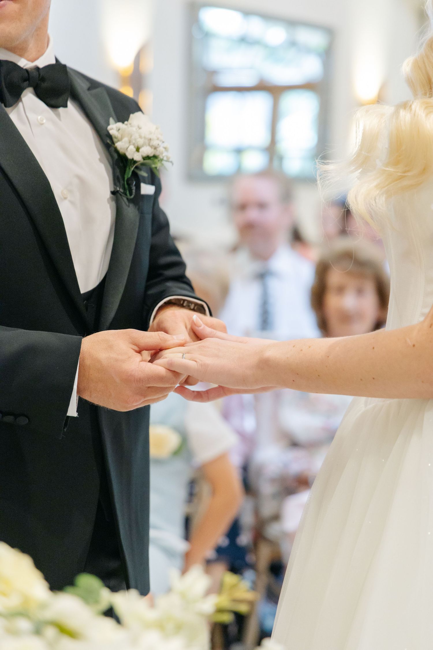 Close-up of wedding ring exchange during ceremony with hands in formal attire.