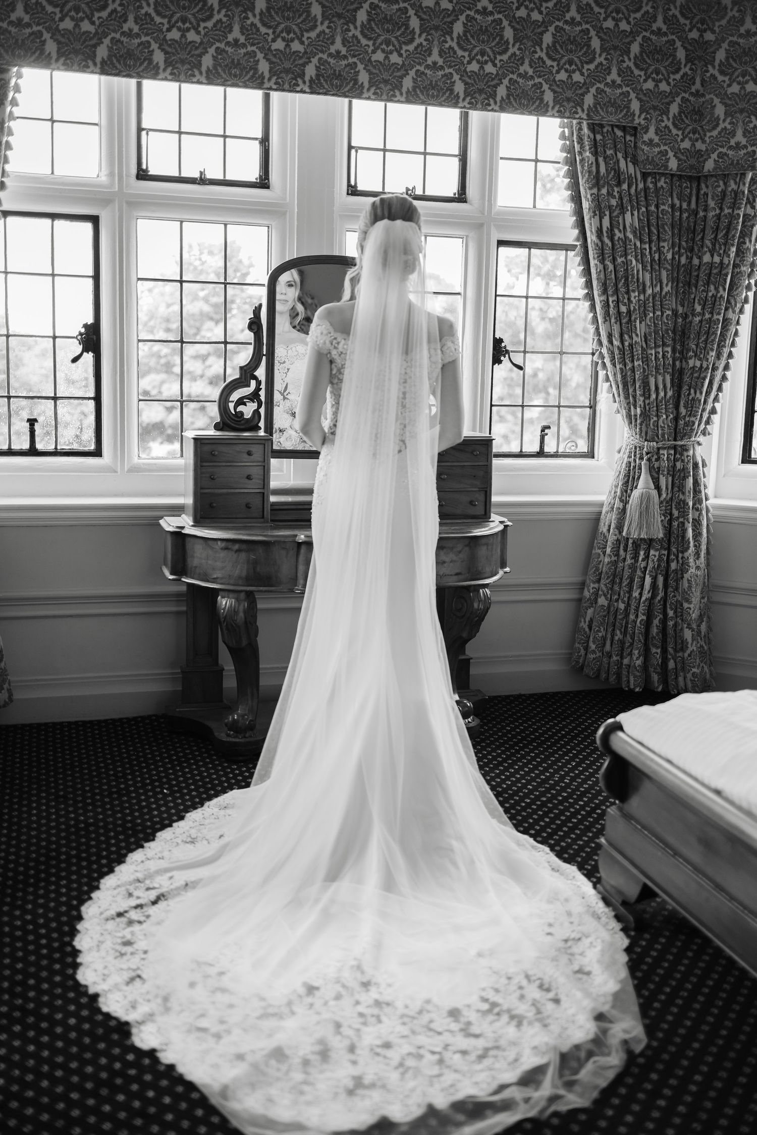 Wedding dress with long flowing train photographed against dark patterned curtains.