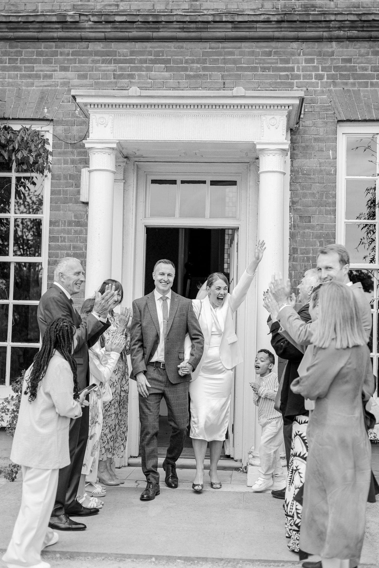 Wedding guests form celebratory receiving line outside brick building with white columns.