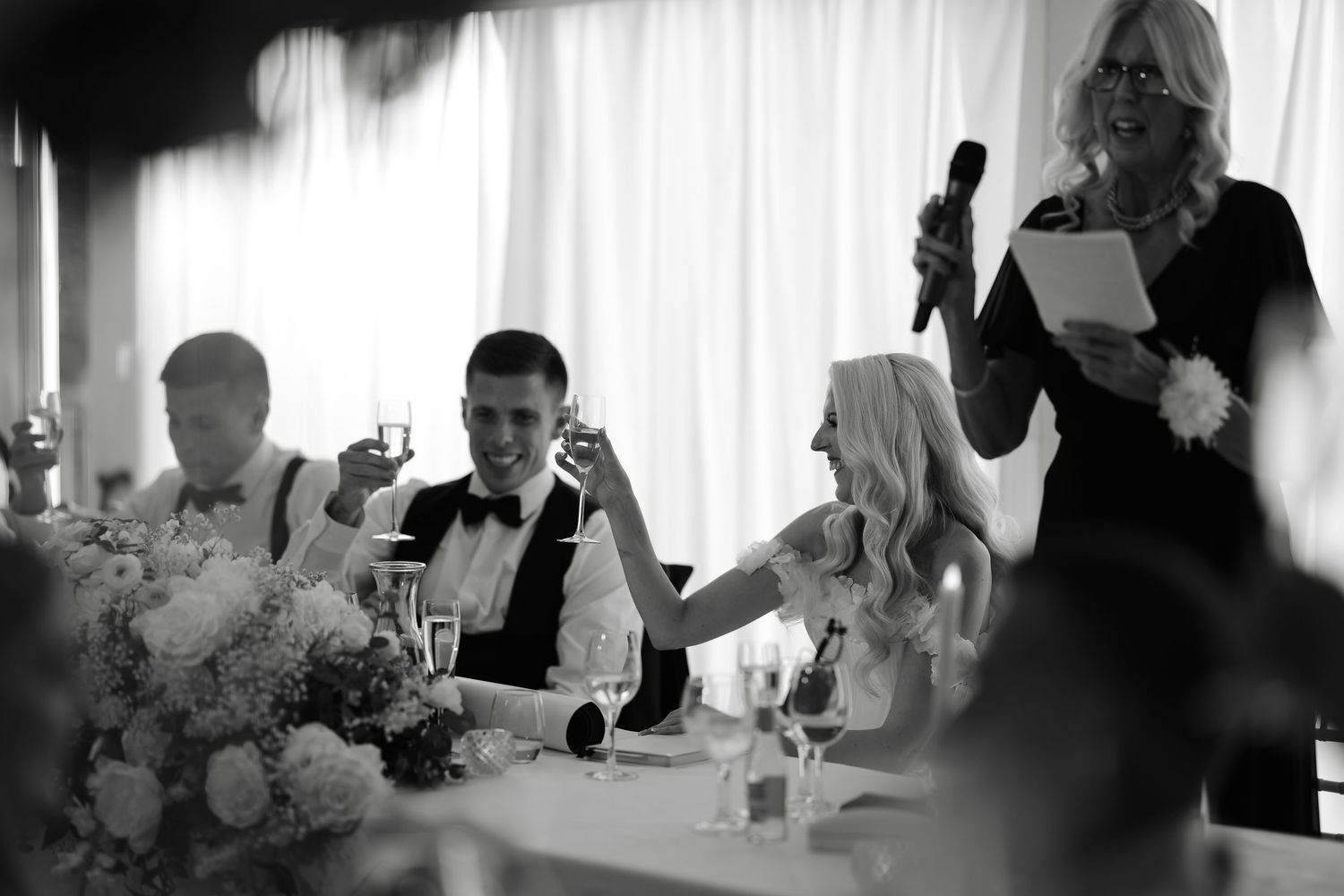 Black and white reception photo showing wedding speeches and table settings.
