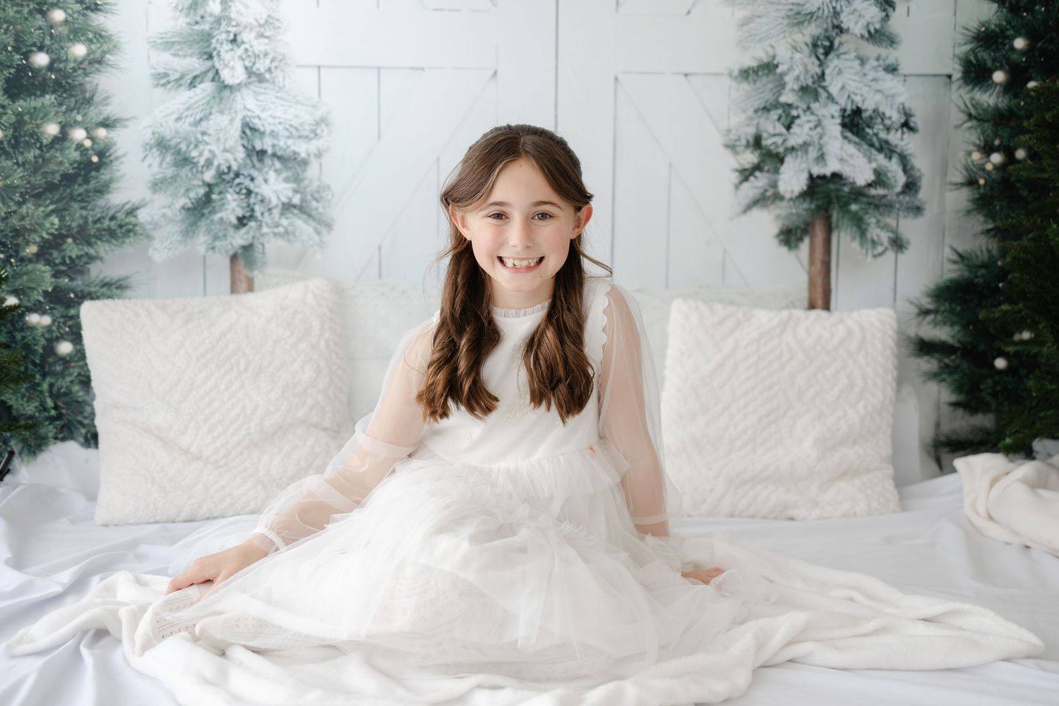 People in white dresses smile and pose together on white bedding with winter decorations.
