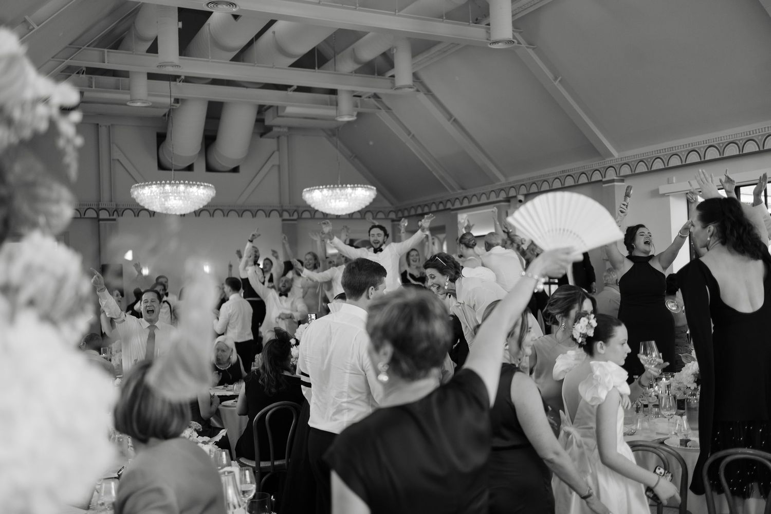 Black and white photo of wedding reception guests dancing and celebrating in an elegant tented venue.