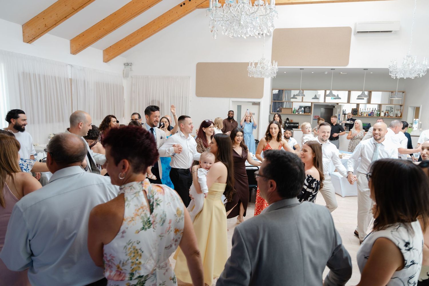 Guests dancing and celebrating in a bright venue with wooden beam ceilings.