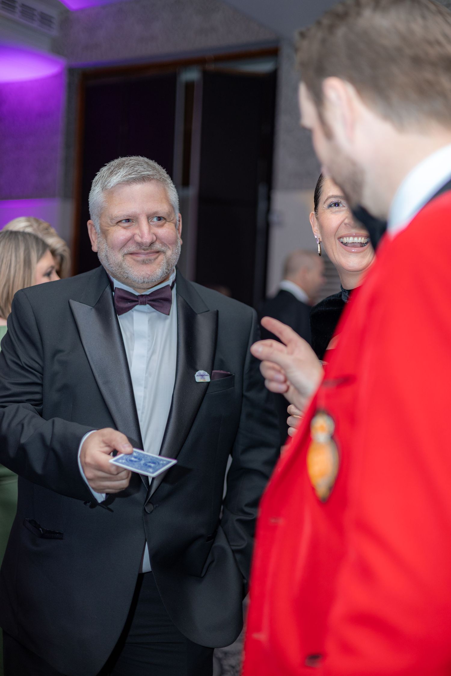 A performer in formal attire shows magic tricks to guests at an upscale party.
