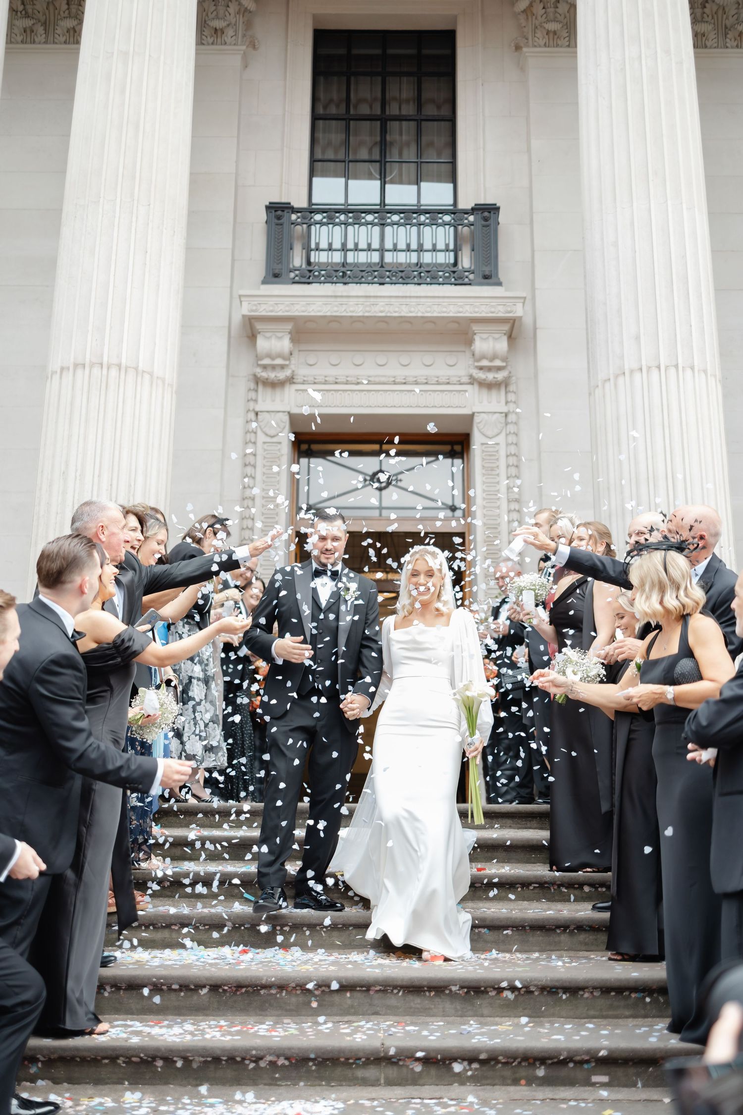 Wedding party celebration with confetti outside a classical building with white columns.