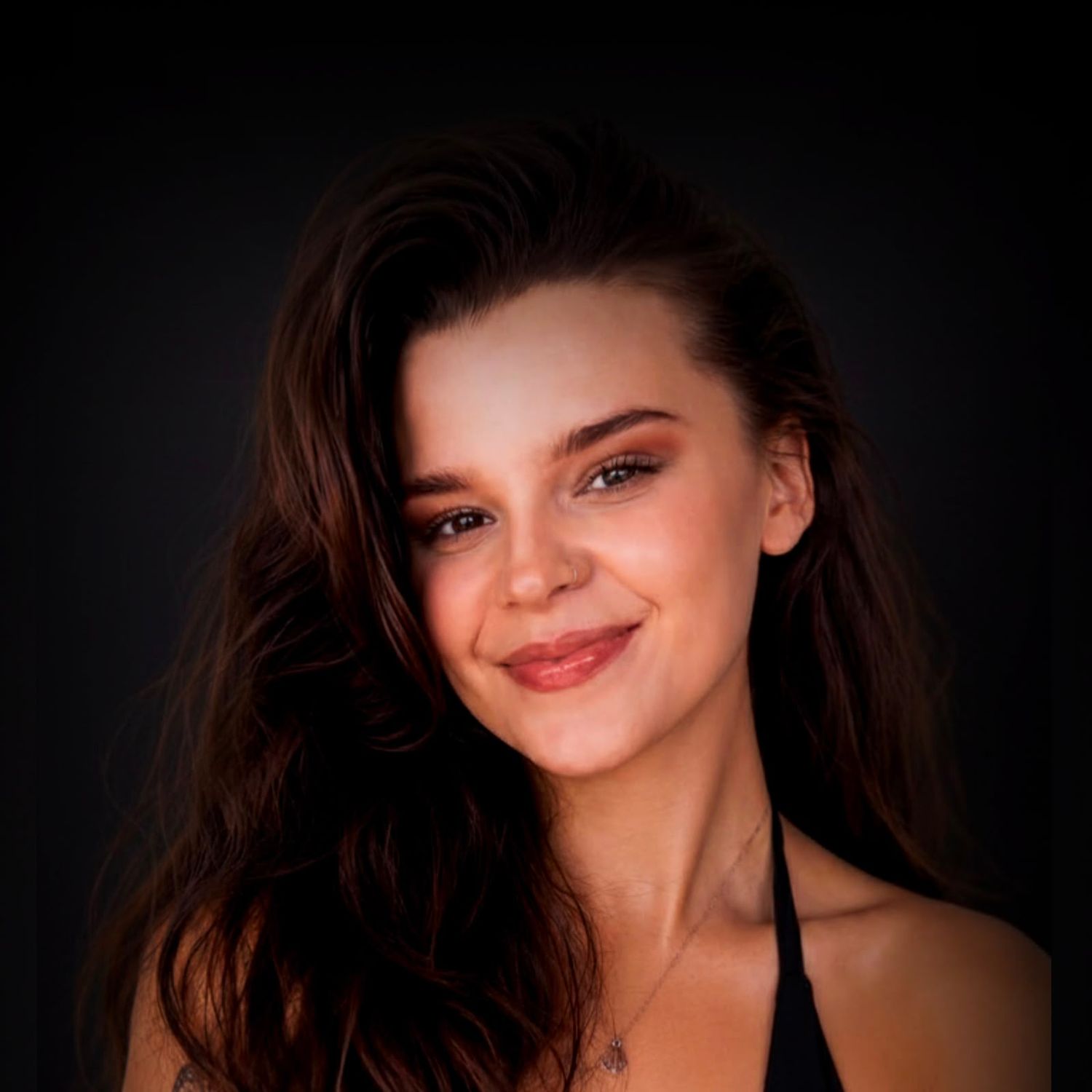 Young woman with long dark hair smiling confidently against a dark background in a professional portrait photo.