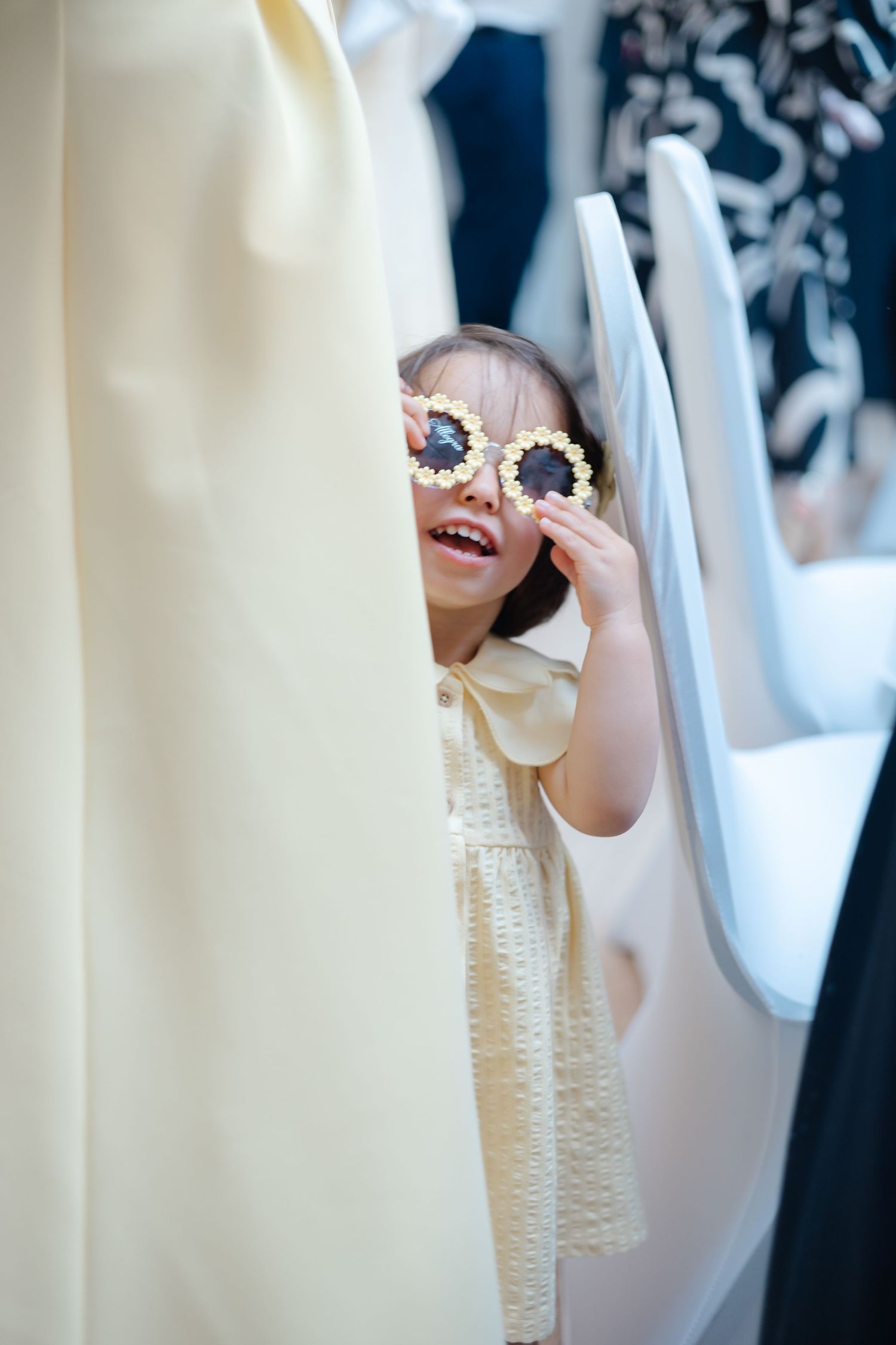 Child in yellow dress plays peek-a-boo during formal event.