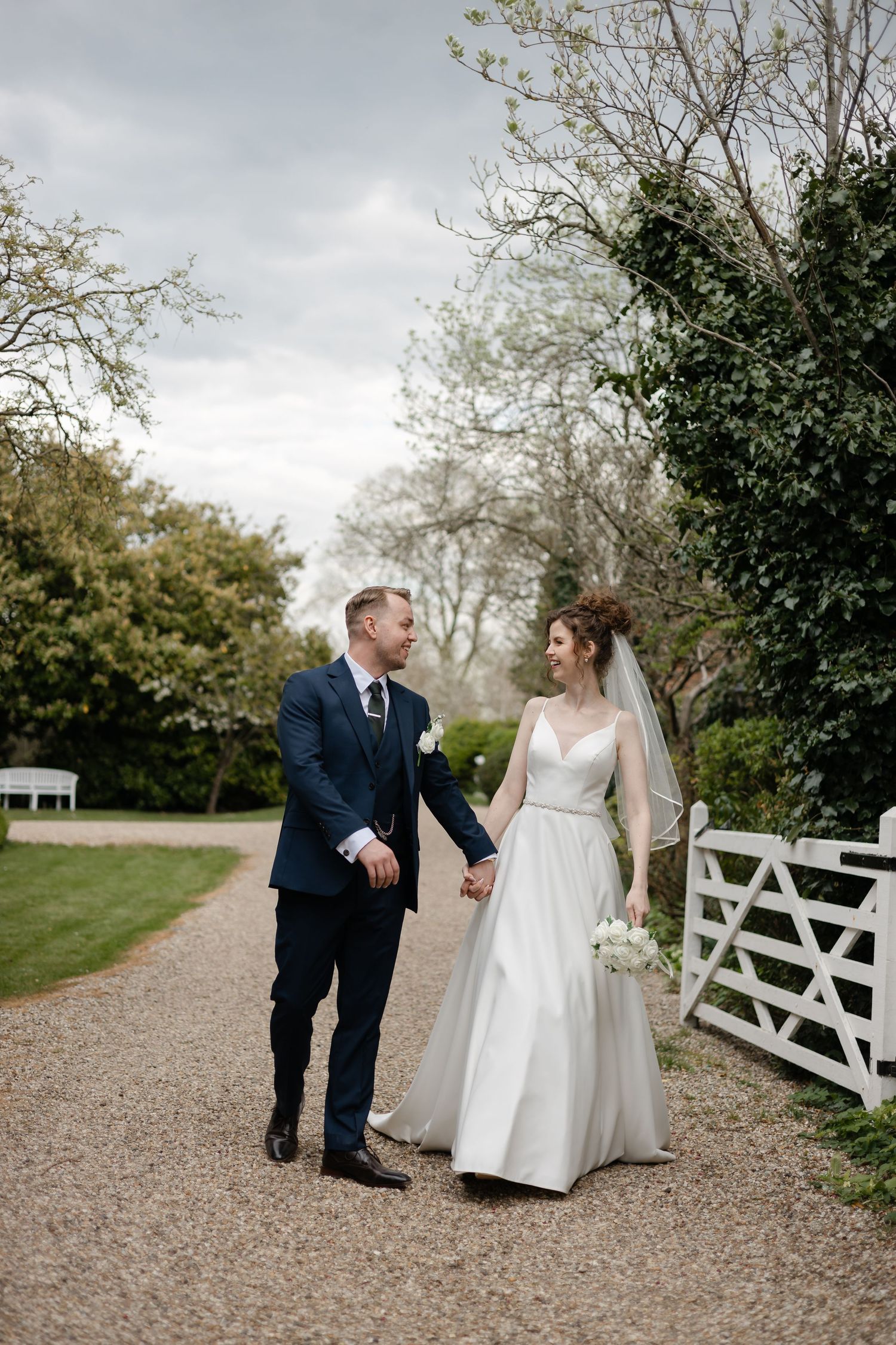 Candid wedding moments captured on gravel path with white fence and natural landscaping.