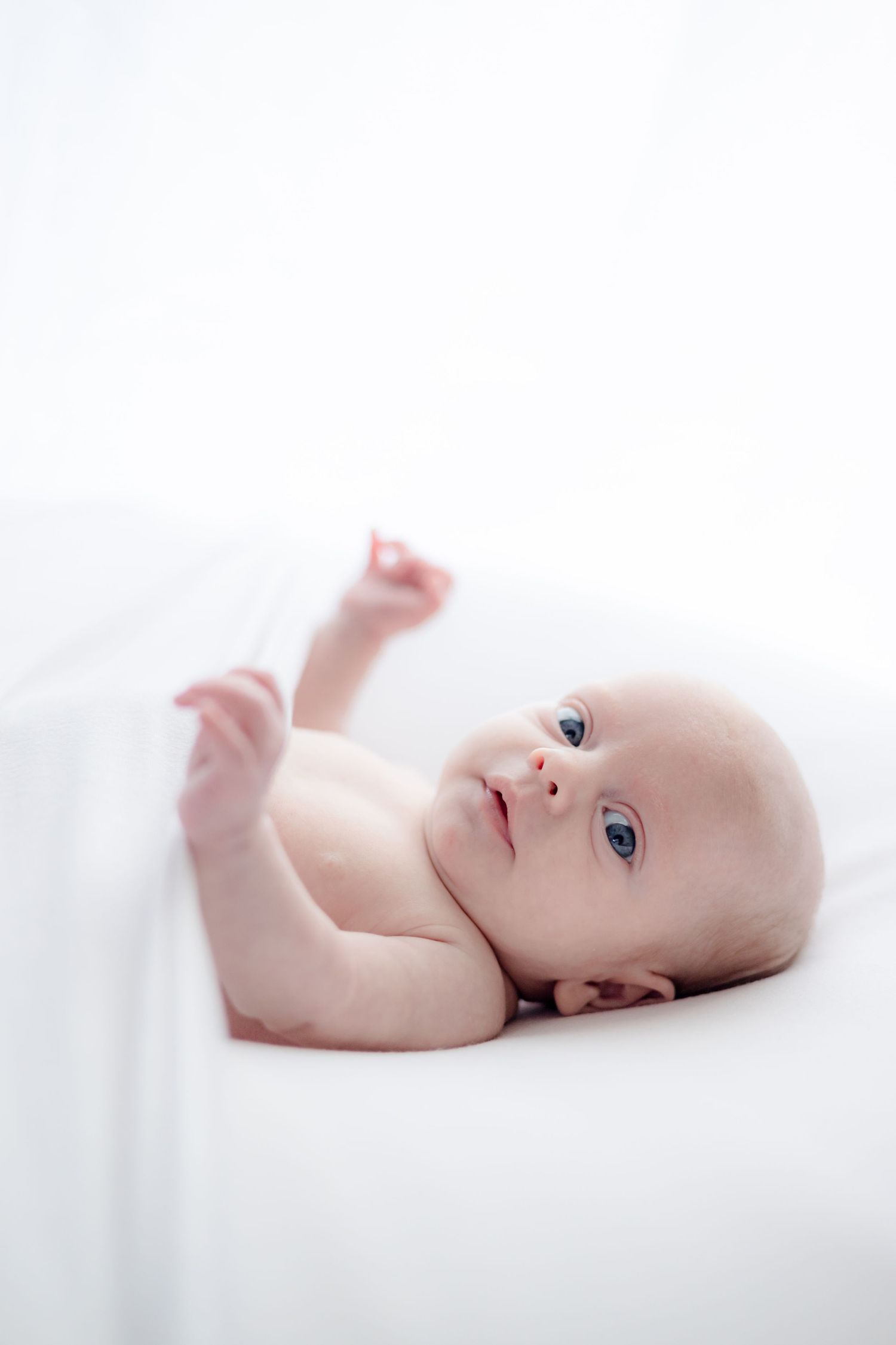 Peaceful newborn baby lying on white blanket with bright blue eyes.