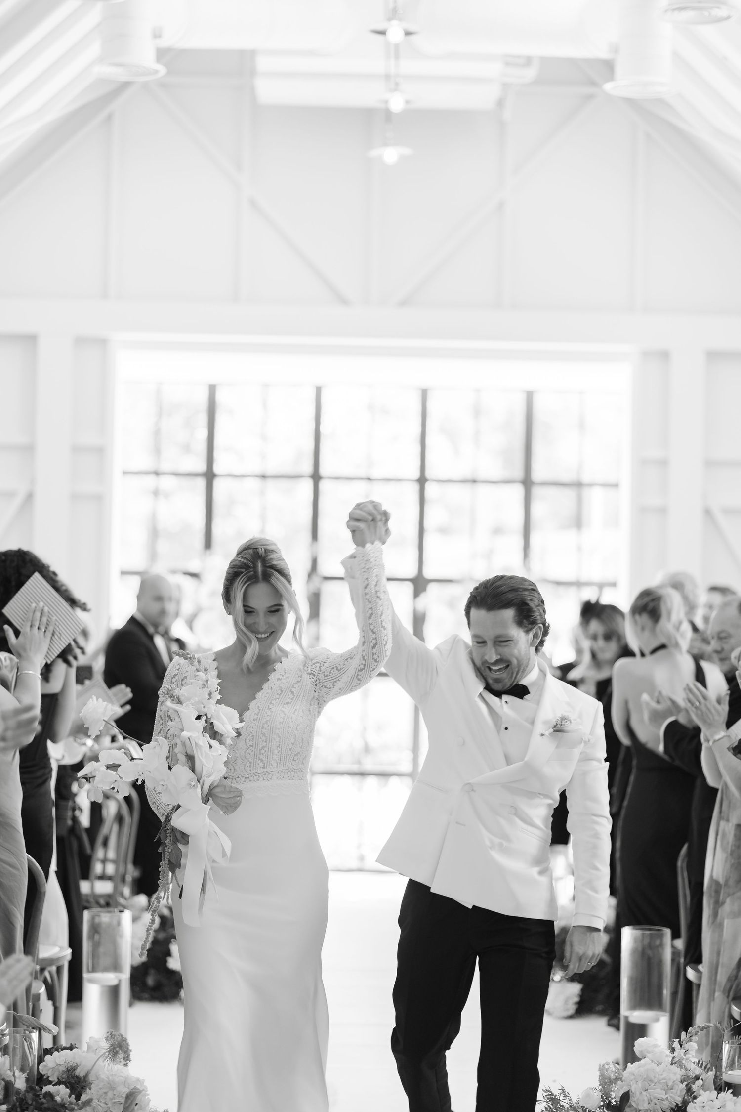 Newlyweds raise joined hands in joy walking down the aisle after their indoor wedding ceremony.