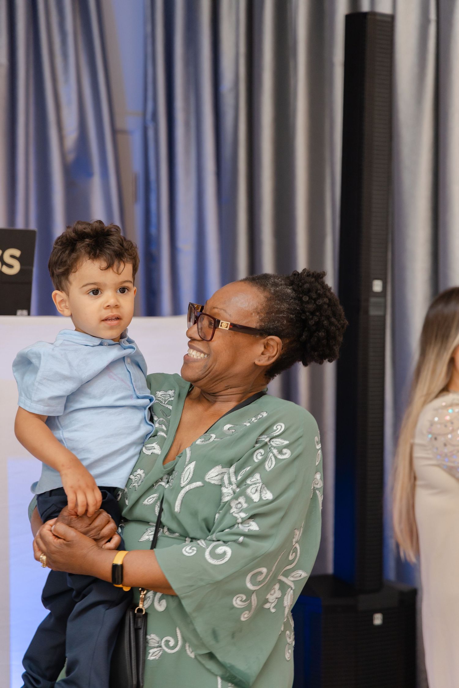 A child in blue shirt shares a happy moment with someone in a green patterned top at an event.