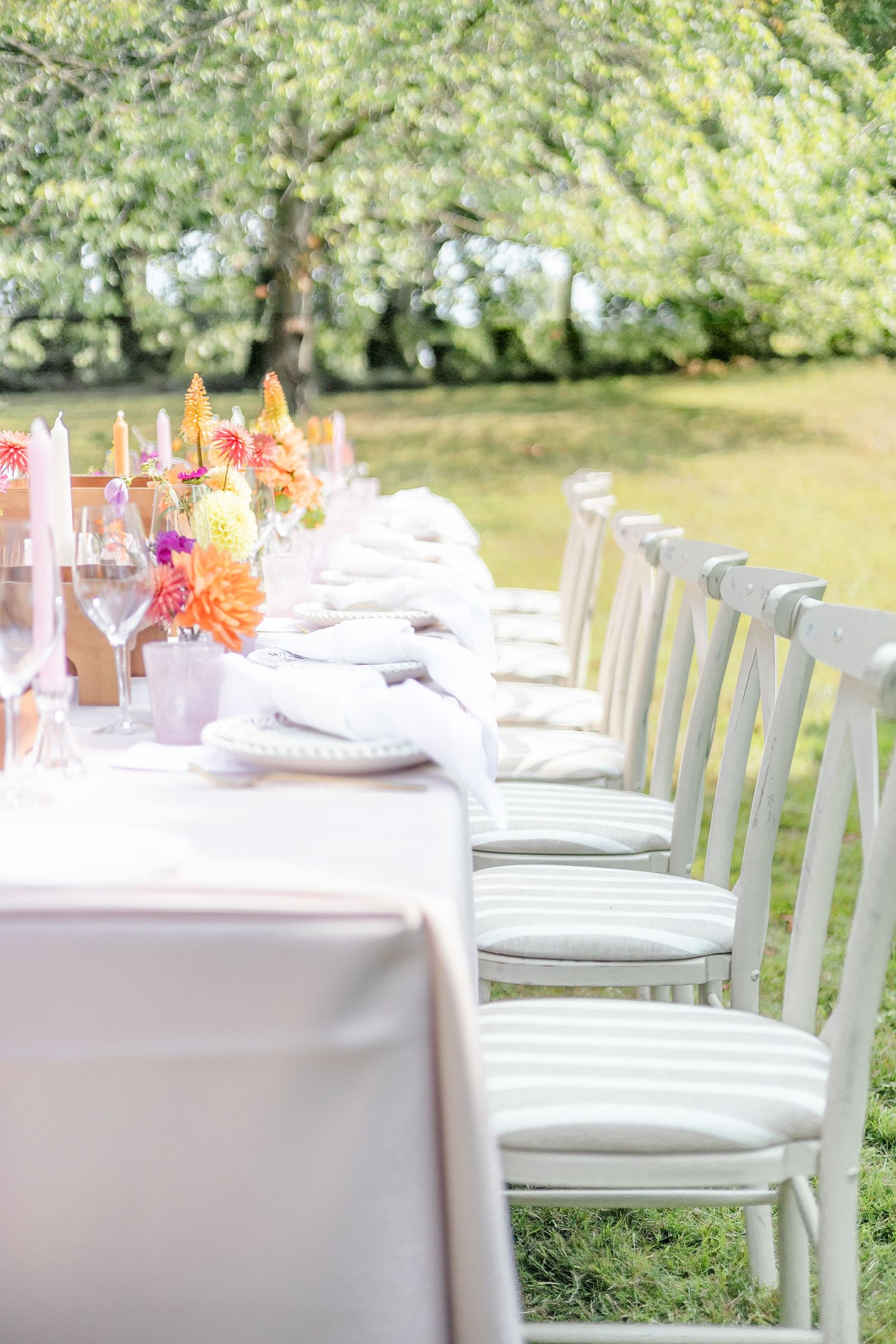 White chairs and tables set up for an elegant outdoor wedding reception with floral centerpieces.